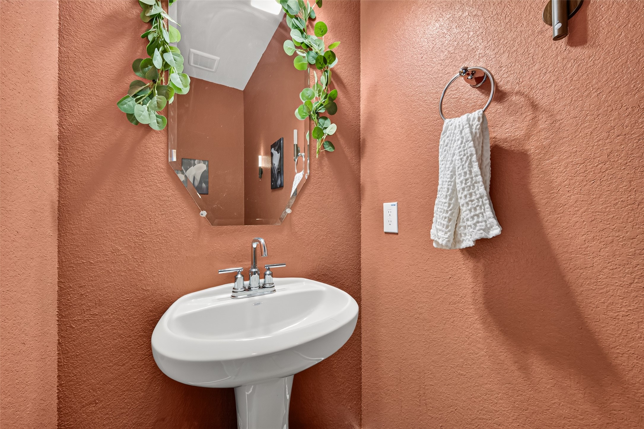 The downstairs half bath features a pedestal sink and a warm accent color.