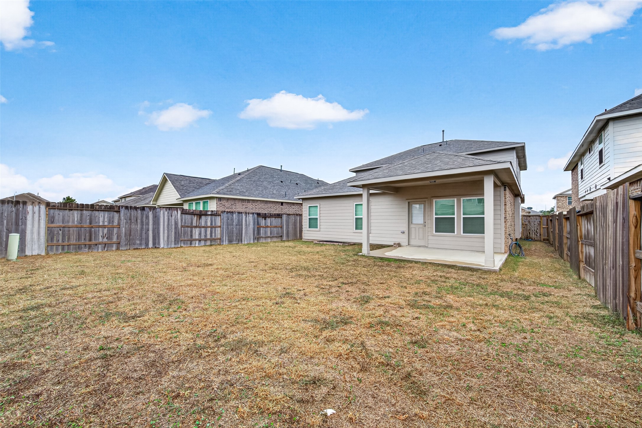 A view across the fenced backyard showcases the rear exterior and covered patio, with open lawn space to enjoy.