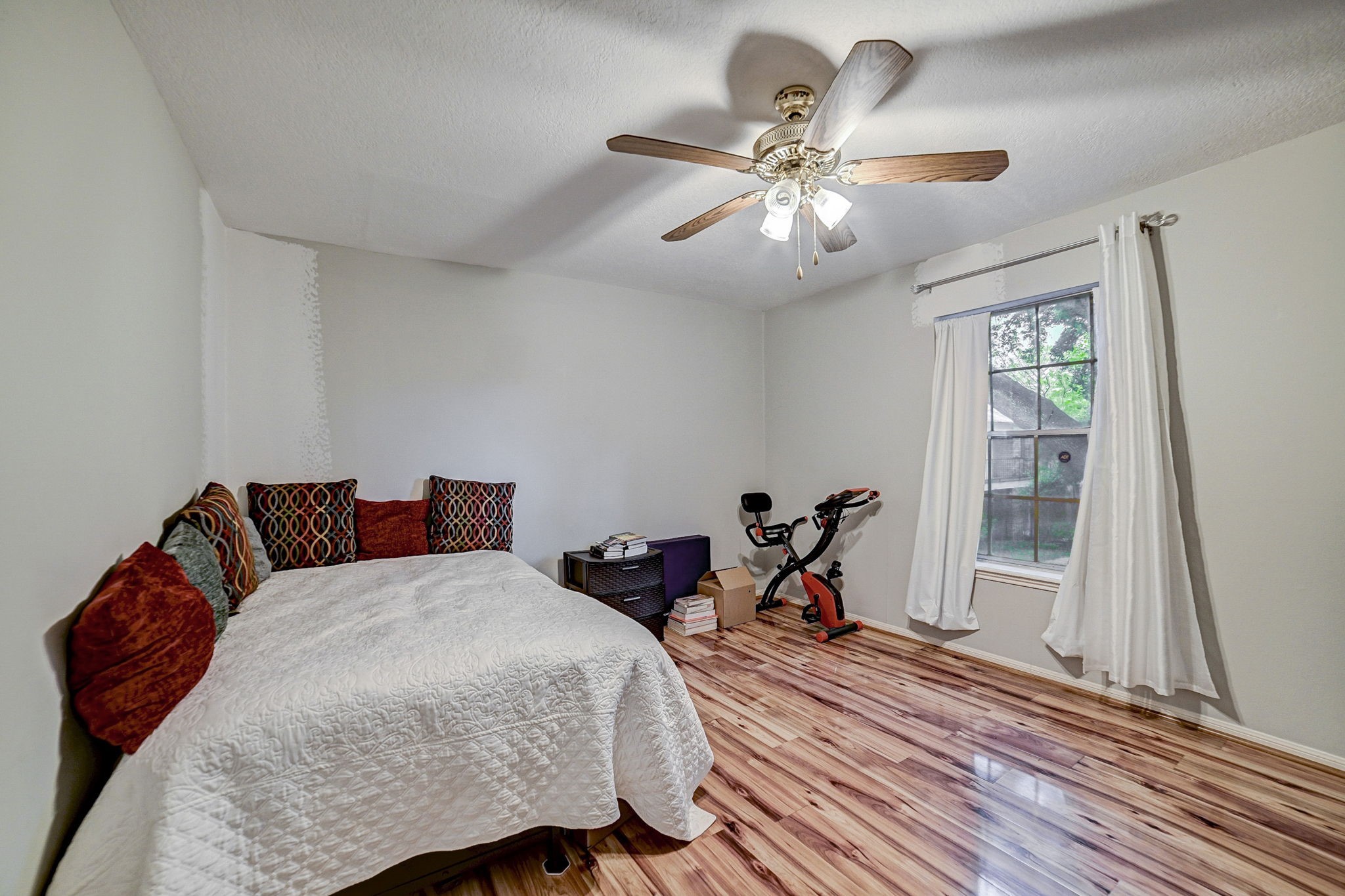 Cozy bedroom with warm wooden flooring, a ceiling fan, and ample natural light streaming through the large window.