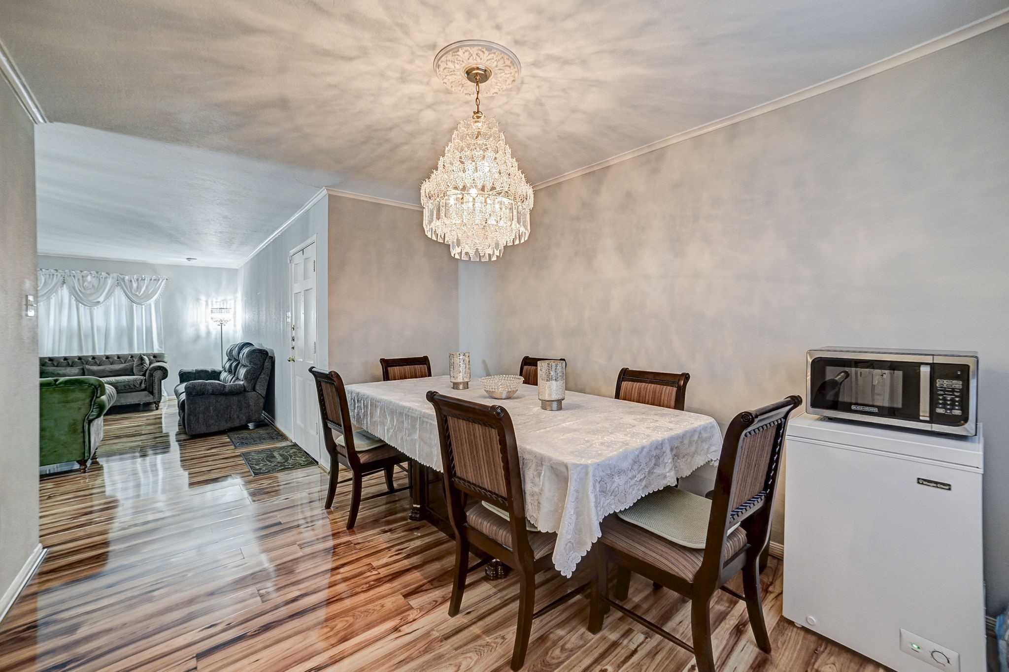 Elegant dining area with a stunning chandelier and rich wood flooring, seamlessly connected to a cozy living space filled with natural light.