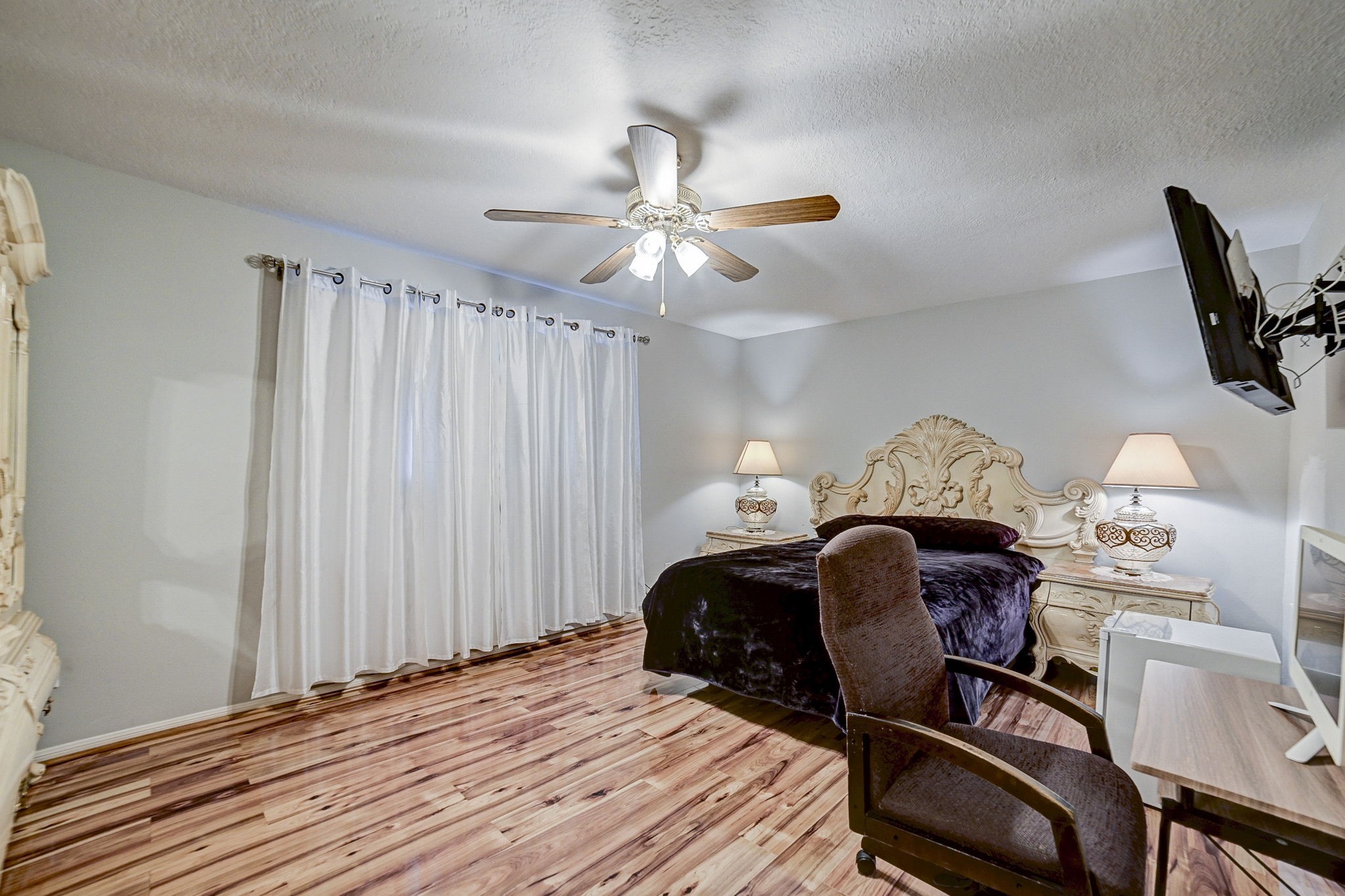 Elegant bedroom features rich wood flooring, a luxurious carved headboard, and soft ambient lighting from stylish bedside lamps.