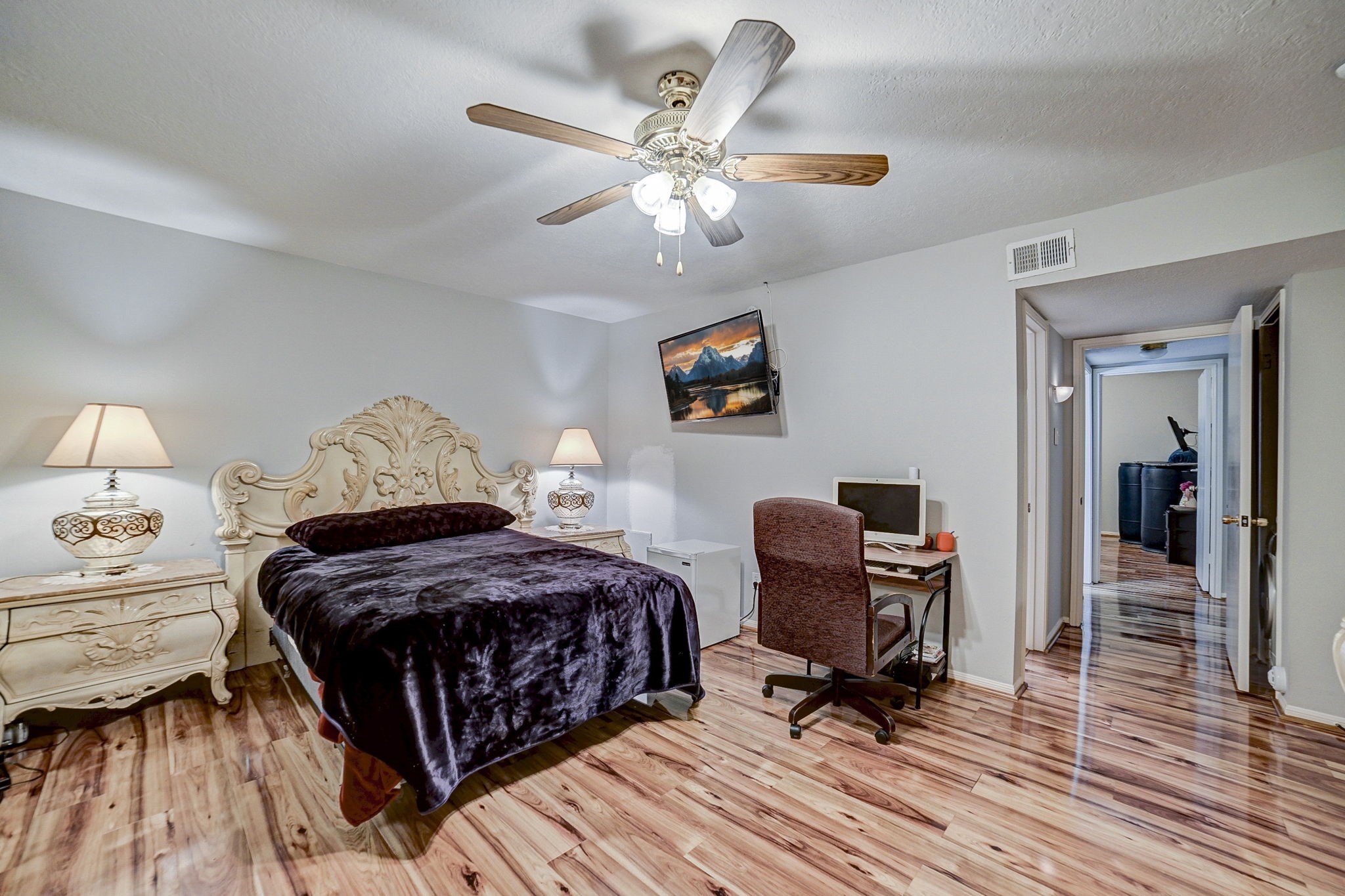 Charming bedroom with elegant carved furniture, warm wood flooring, and a cozy workspace, all illuminated by soft lighting and a ceiling fan.