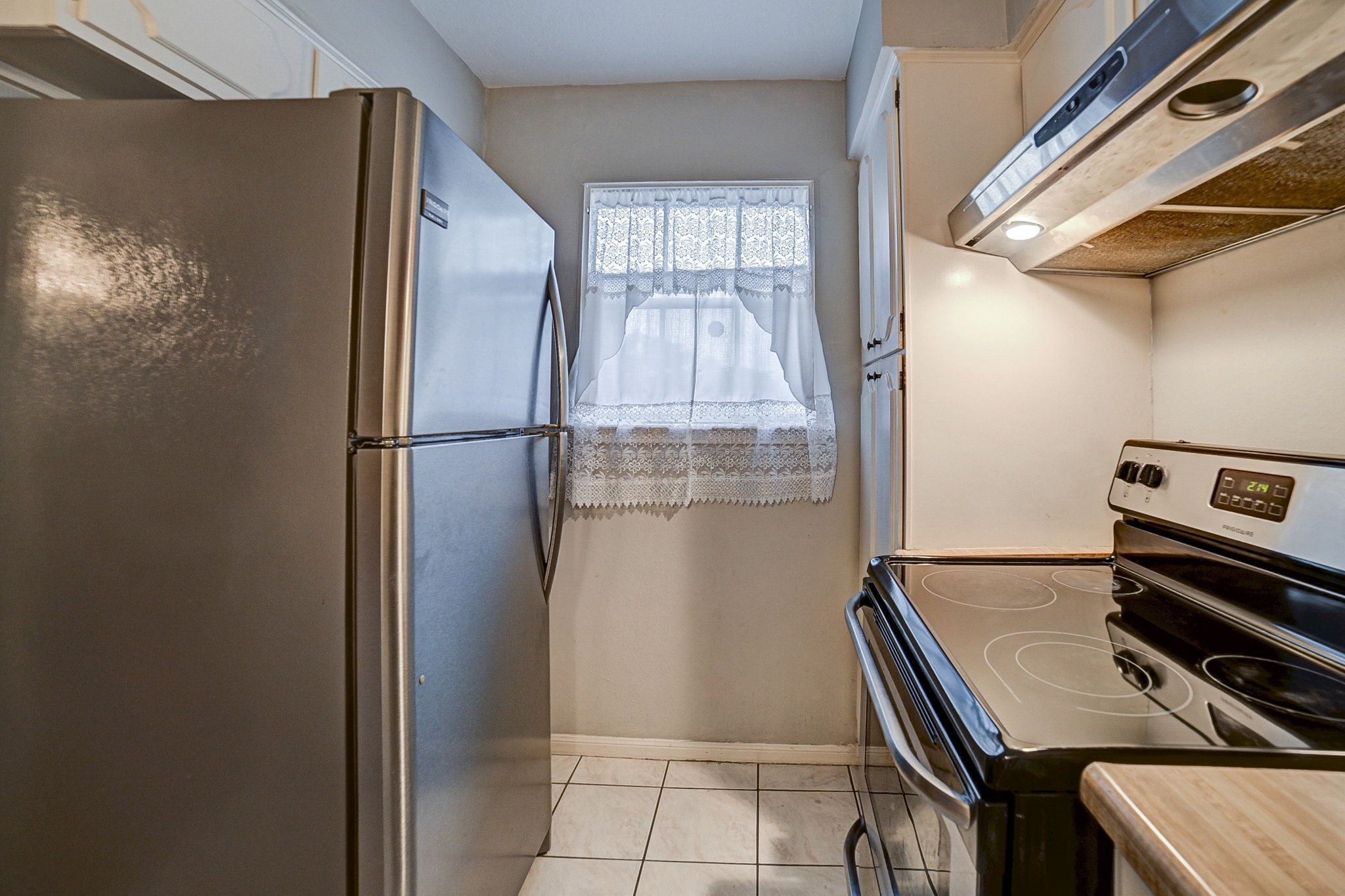 Cozy kitchen featuring a sleek stainless steel refrigerator and modern electric stove, complemented by a charming window with lace curtains for natural light.