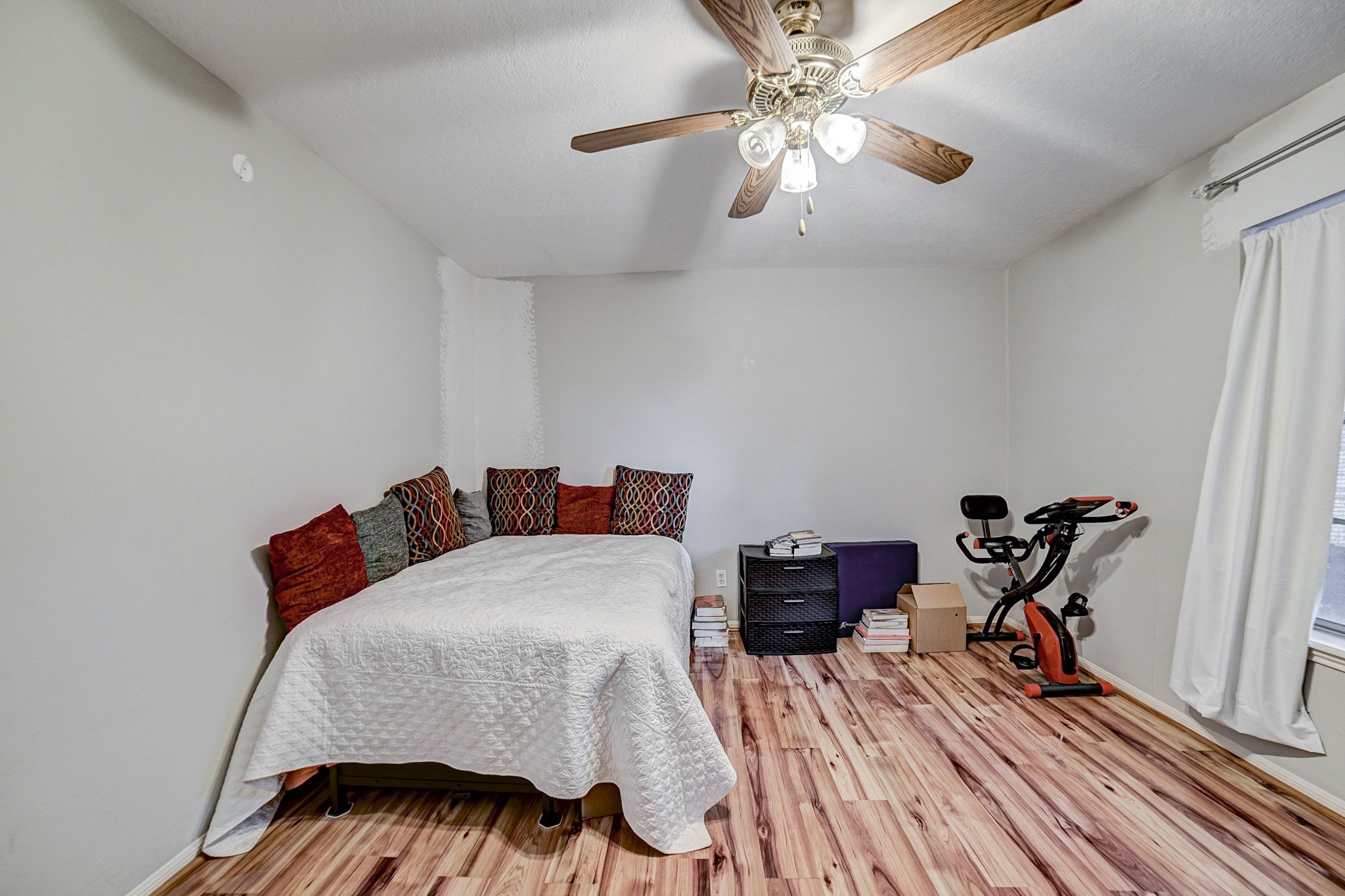 Cozy bedroom with warm wood flooring, ceiling fan, and plenty of natural light, perfect for relaxation or a home gym setup.