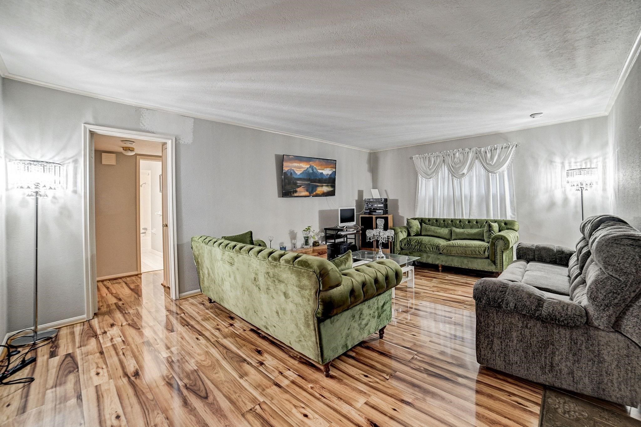 Spacious living room with elegant hardwood floors, plush seating in rich greens and grays, and abundant natural light filtering through stylish drapes. Spacious living room with elegant hardwood floors, plush seating in rich greens and grays, and abundant natural light filtering through stylish drapes.