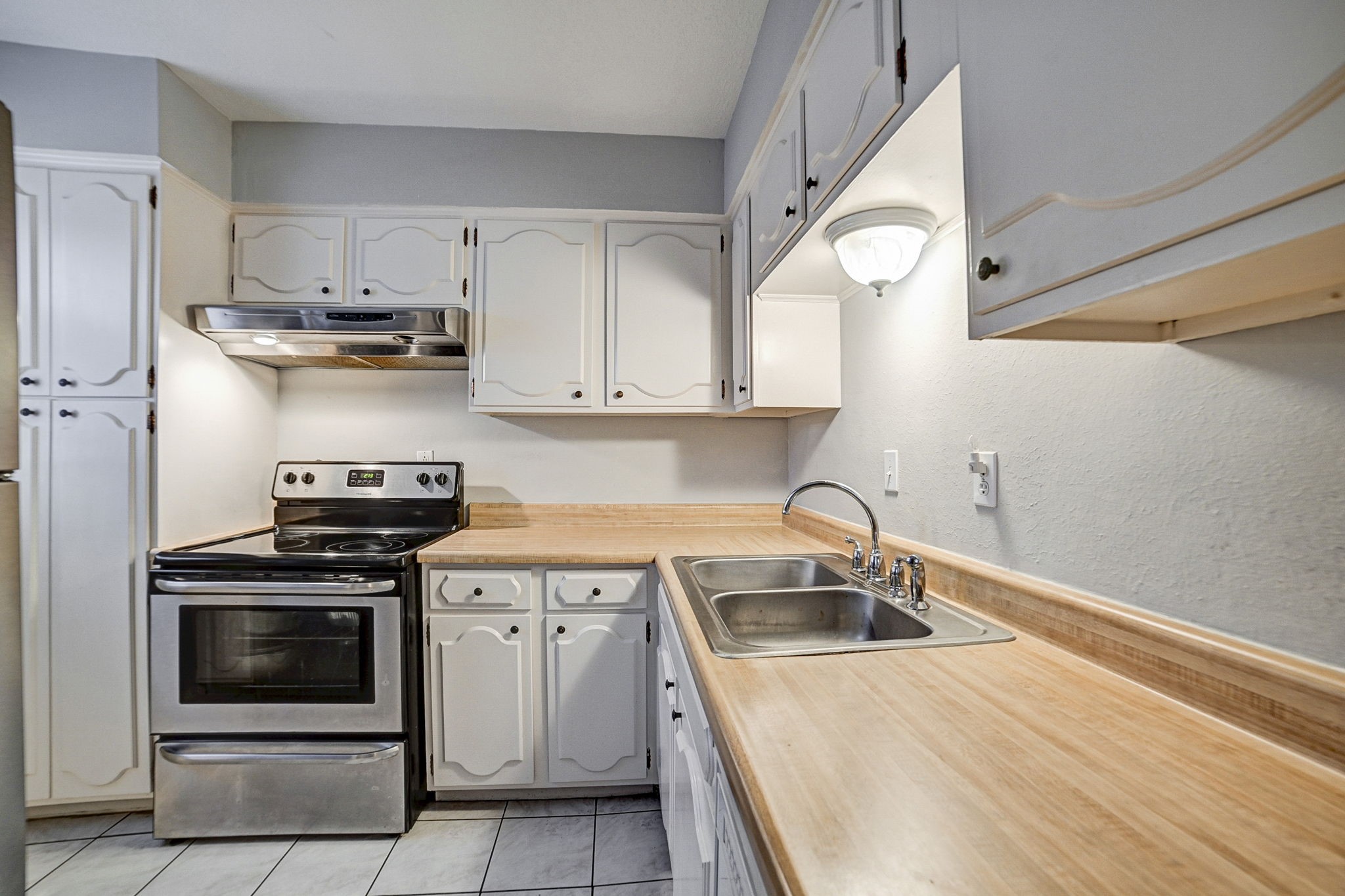 Charming kitchen featuring white cabinetry, a sleek stainless steel electric stove, and a spacious countertop with an integrated sink for convenient meal prep.
