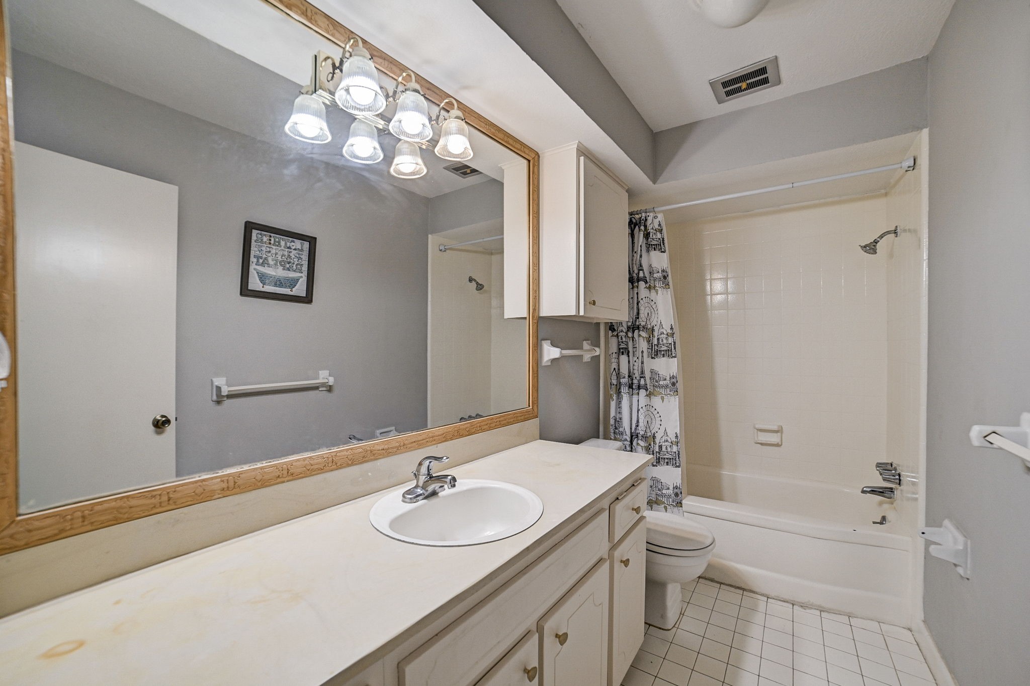 Bright bathroom featuring a large mirror, ample counter space, and a shower-tub combo with a decorative curtain.