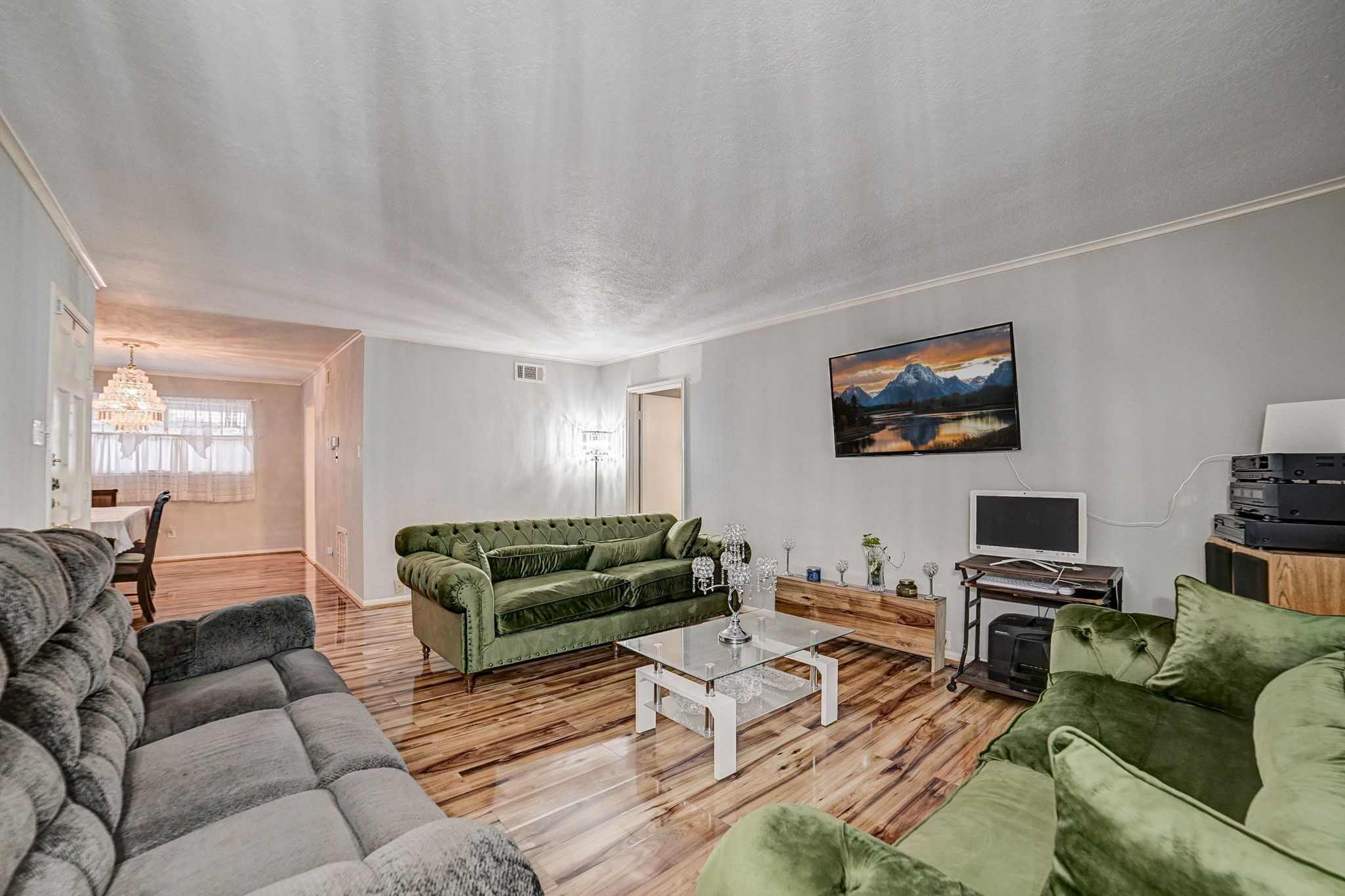 Spacious living room with elegant wood flooring, stylish green and gray sofas, and a mounted flat-screen TV, creating a cozy and inviting atmosphere. Spacious living room with elegant wood flooring, stylish green and gray sofas, and a mounted flat-screen TV, creating a cozy and inviting atmosphere.