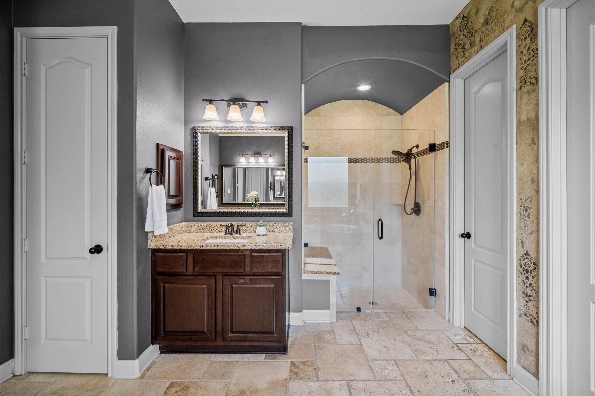 The primary bath offers a frameless shower with a bench and separate vanity areas on one side.