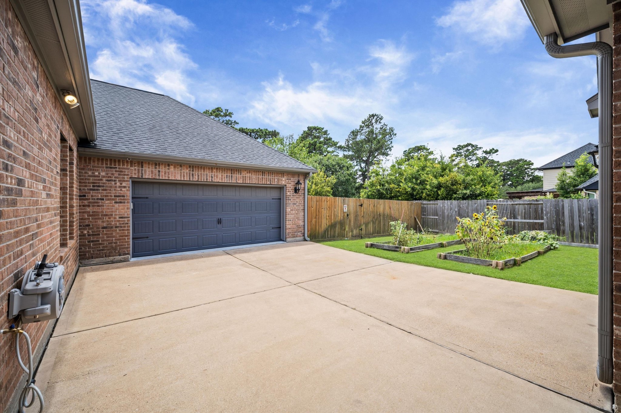 A retractable garden hose rests on the left side of the driveway for reaching the planter boxes.