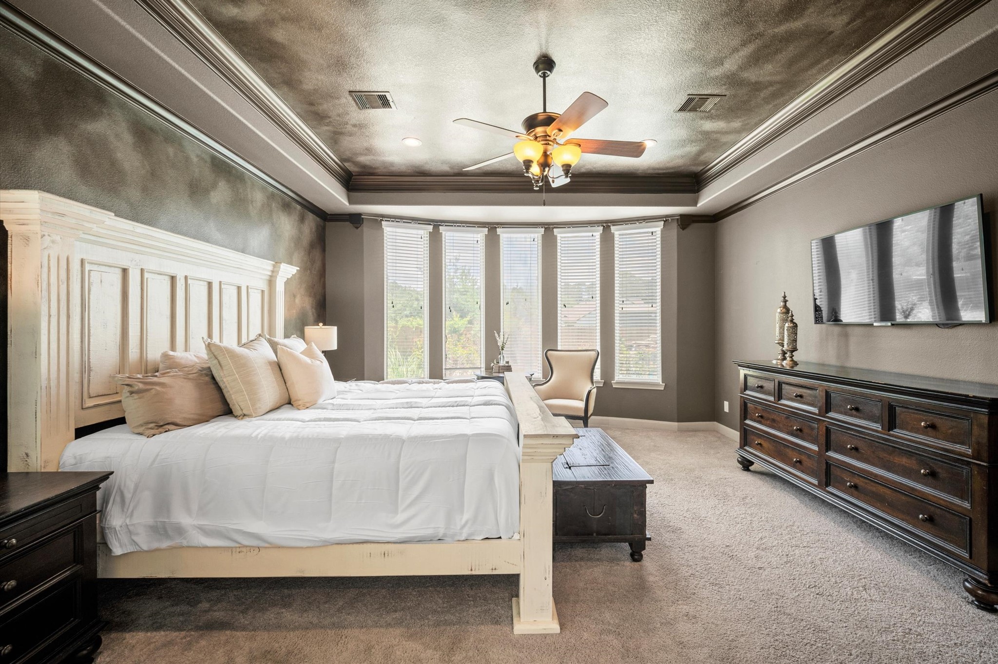 An incredible primary suite offers a tray ceiling, a wall of windows, and plenty of space for a king-sized bed, side tables, and even a sitting area.