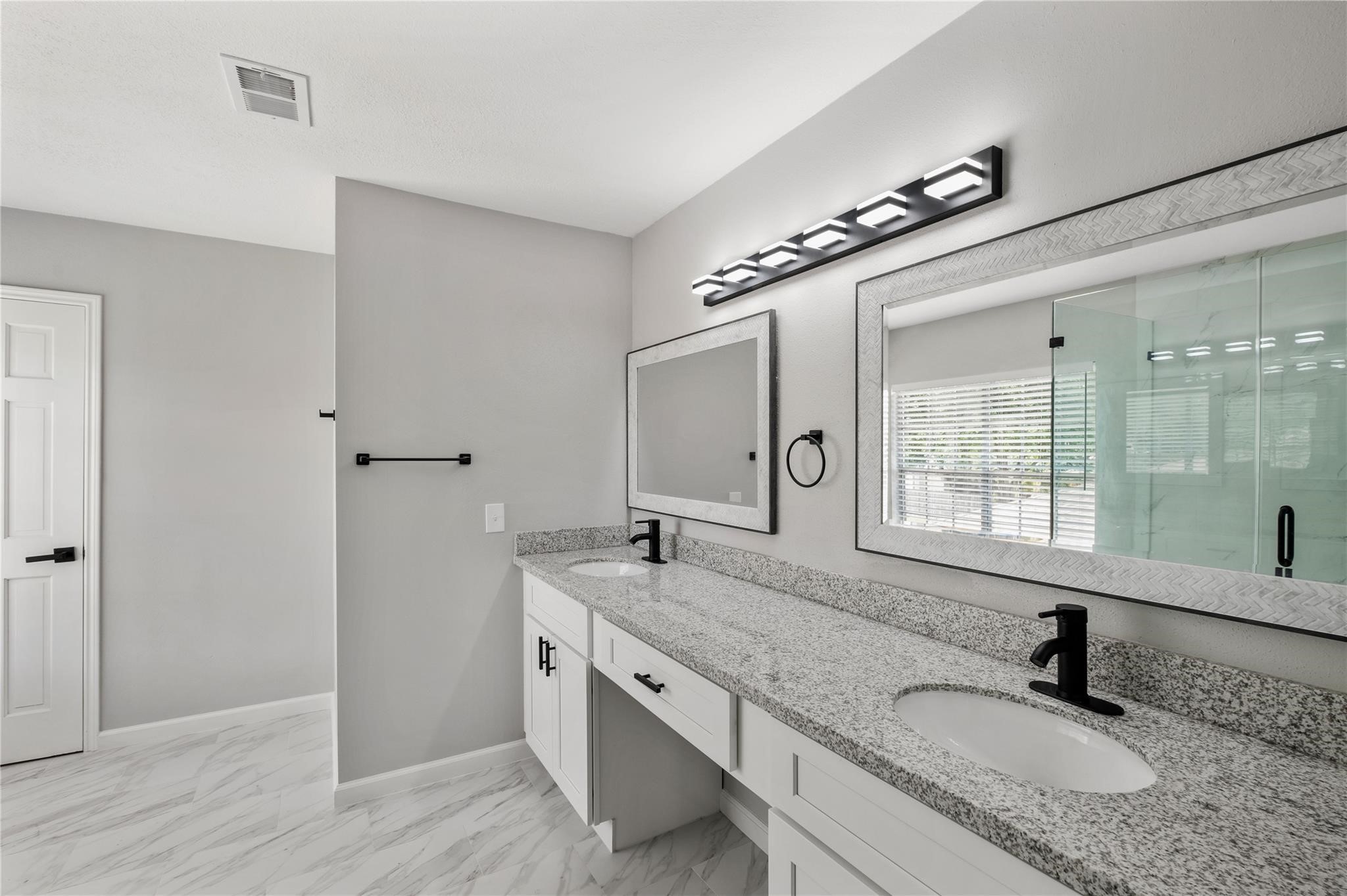 The renovated primary bathroom features dual sinks, granite countertops, updated fixtures, and a spacious walk-in shower.