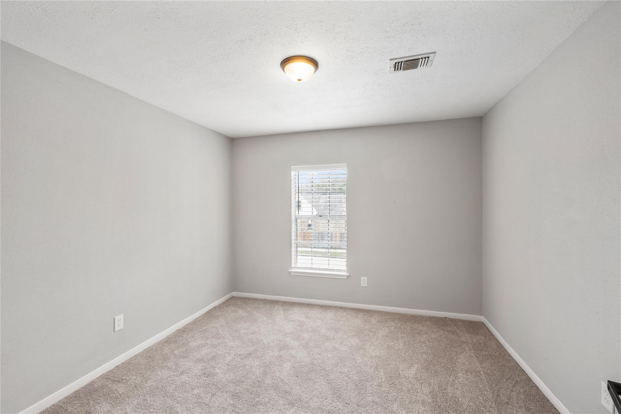The third bedroom offers comfortable accommodations with soft carpeting, natural light, and a neutral color palette.
