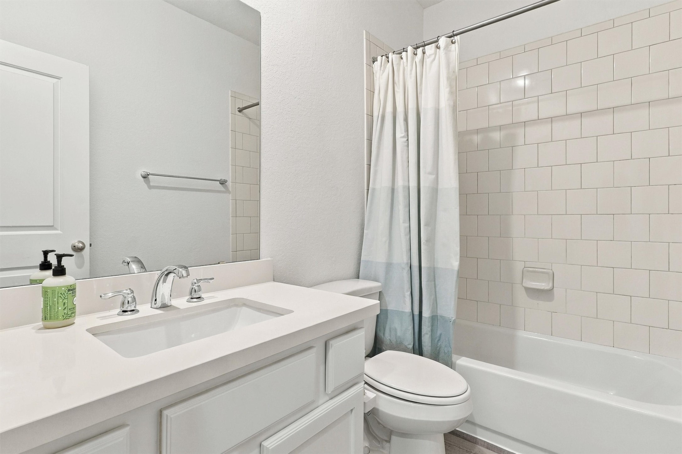 Second full bath, beautifully done in white tile and timeless silver accents. This bathroom features solid surface countertop and undermount sink, white vanity, and shower/tub combo!