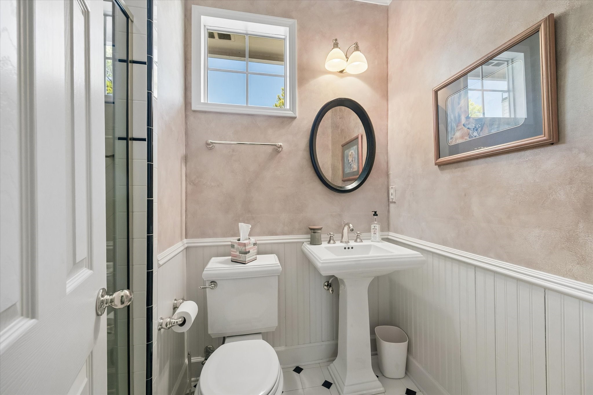 An additional full bathroom adds convenience and flexibility to the spacious addition above the garage. Tucked away for convenience, this charming bathroom features classic wainscoting, a pedestal sink, and a separate shower.