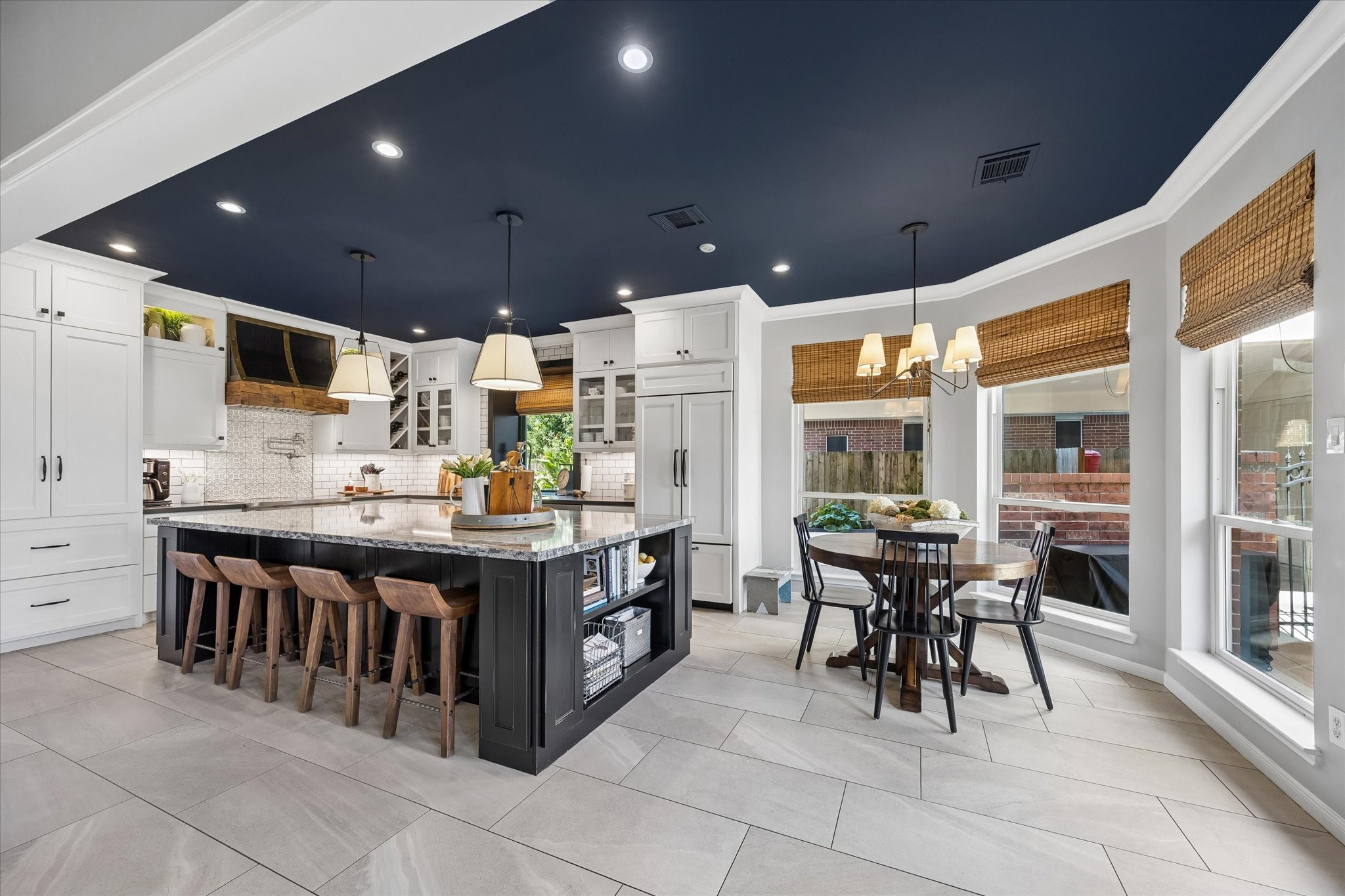Thoughtful design details make this space truly stand out. A dramatic contrasting ceiling, elegant pendant lighting, woven window shades, and expansive windows overlooking the backyard bring warmth and character to the room. The beautiful combination of finishes creates a space that feels both sophisticated and comfortable for everyday living.