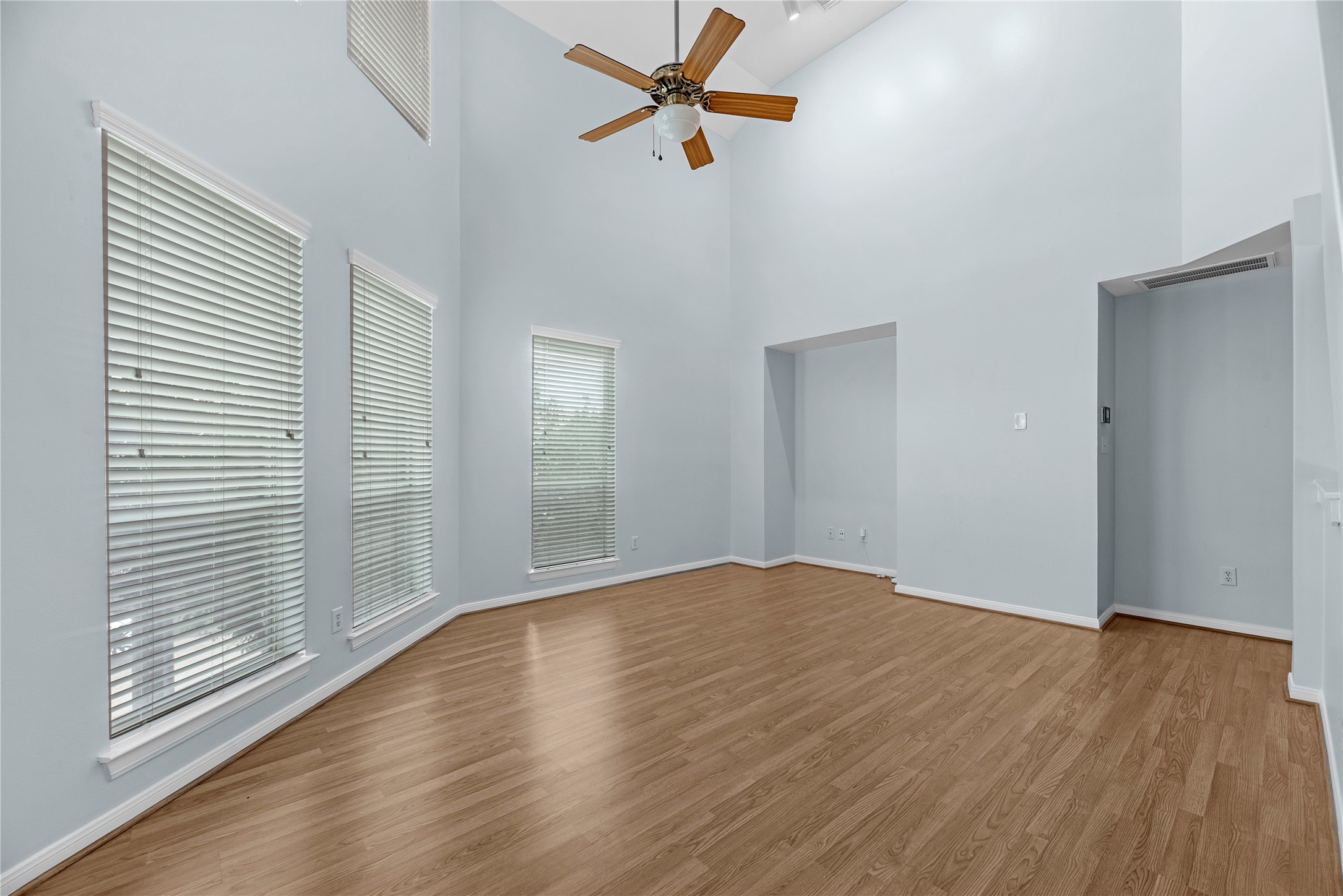 Natural light fills the living area through large windows with plantation shutters, while high ceilings, updated flooring, and a ceiling fan create a bright and comfortable gathering space.