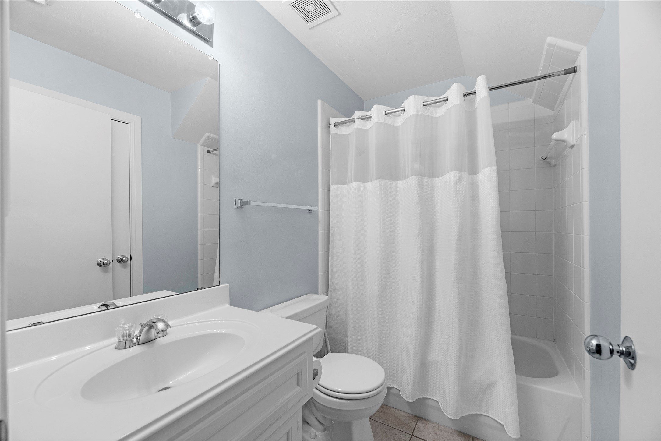 The en suite guest bathroom features a clean, functional design with white cabinetry, a single-sink vanity, tile flooring, and a tub/shower combination. Conveniently connected to the first-floor guest suite, it provides a private full bath for guests.