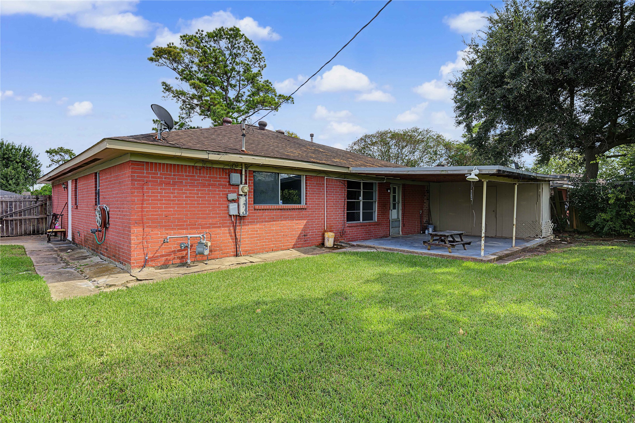 Spacious backyard view featuring a covered patio, mature shade tree, and plenty of green space.