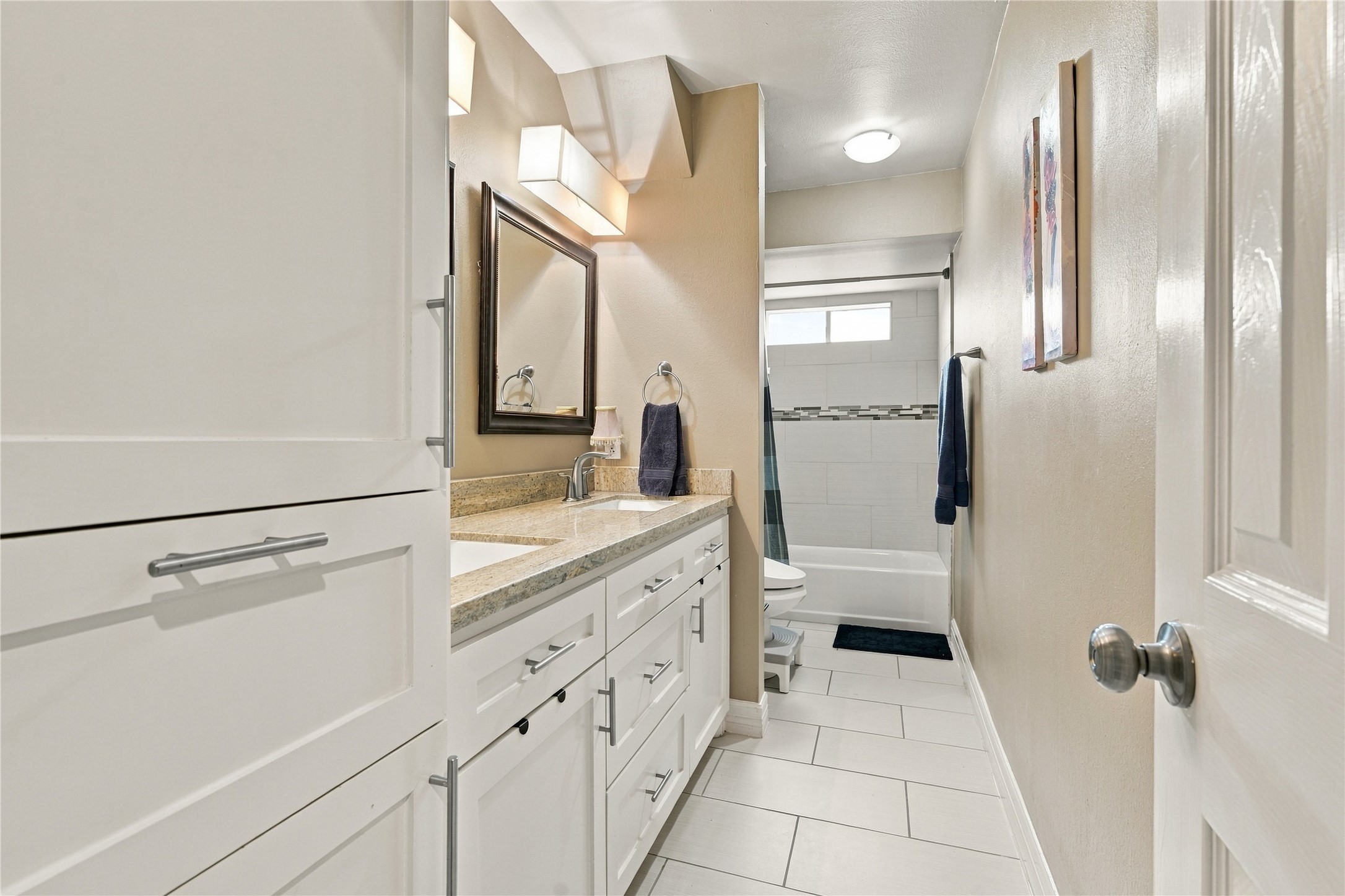 This secondary full bath features a white shaker vanity, a granite countertop & tall linen cabinet. The tub/shower combination is finished in white tile with a mosaic accent band.