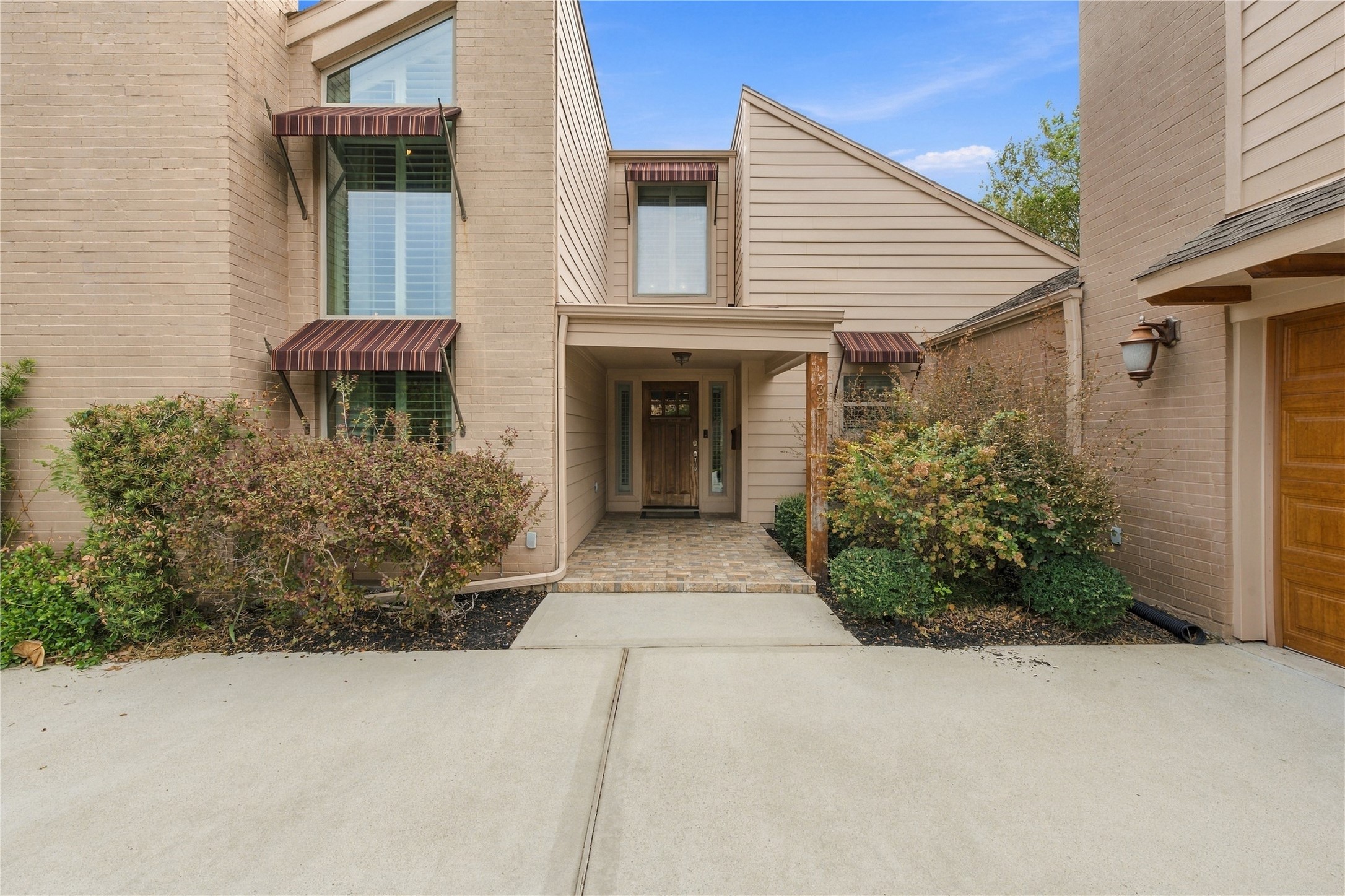 Covered entry features a brick-paver landing, solid wood front door w/ glass sidelights & tall windows topped by striped awnings on either side.