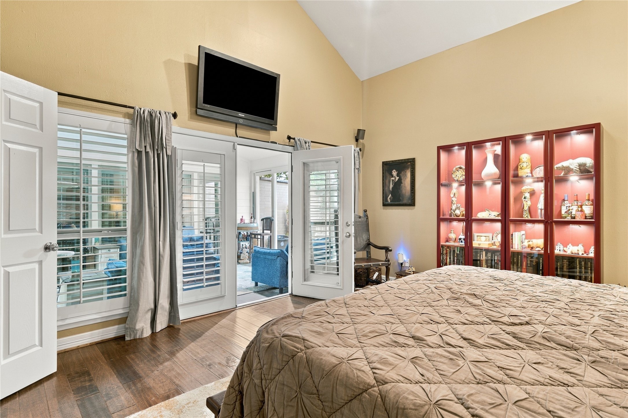 Shuttered French doors & matching windows line one wall of the primary, with a view through the sunroom to the patio beyond. Natural light pours in, and the shutters close for privacy anytime.