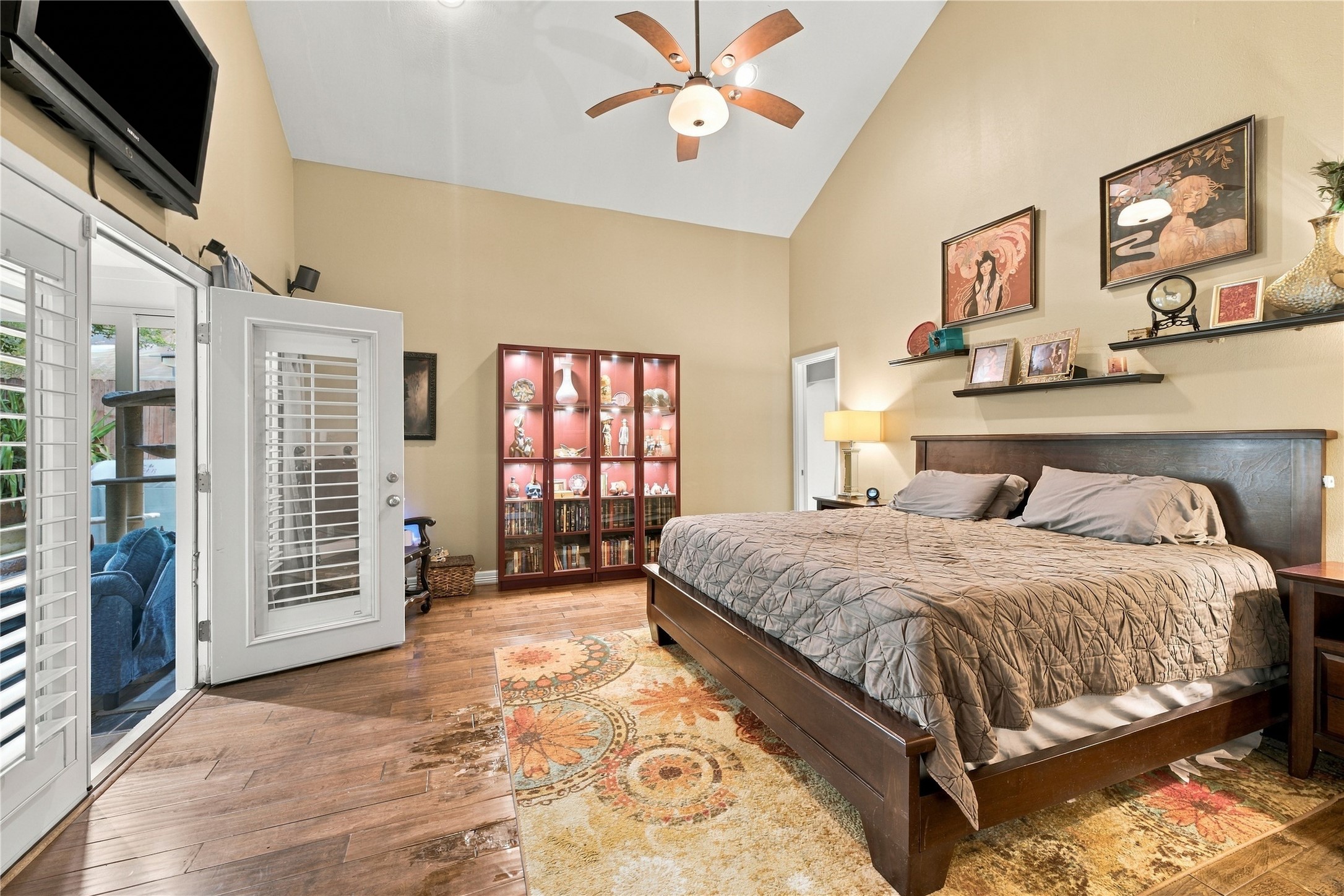 Spacious primary bedroom features a dramatic vaulted ceiling, and rich wood floors, offering a private retreat. A doorway on the back wall leads to the en-suite bath & walk-in closet, the perfect space to relax after a long day.