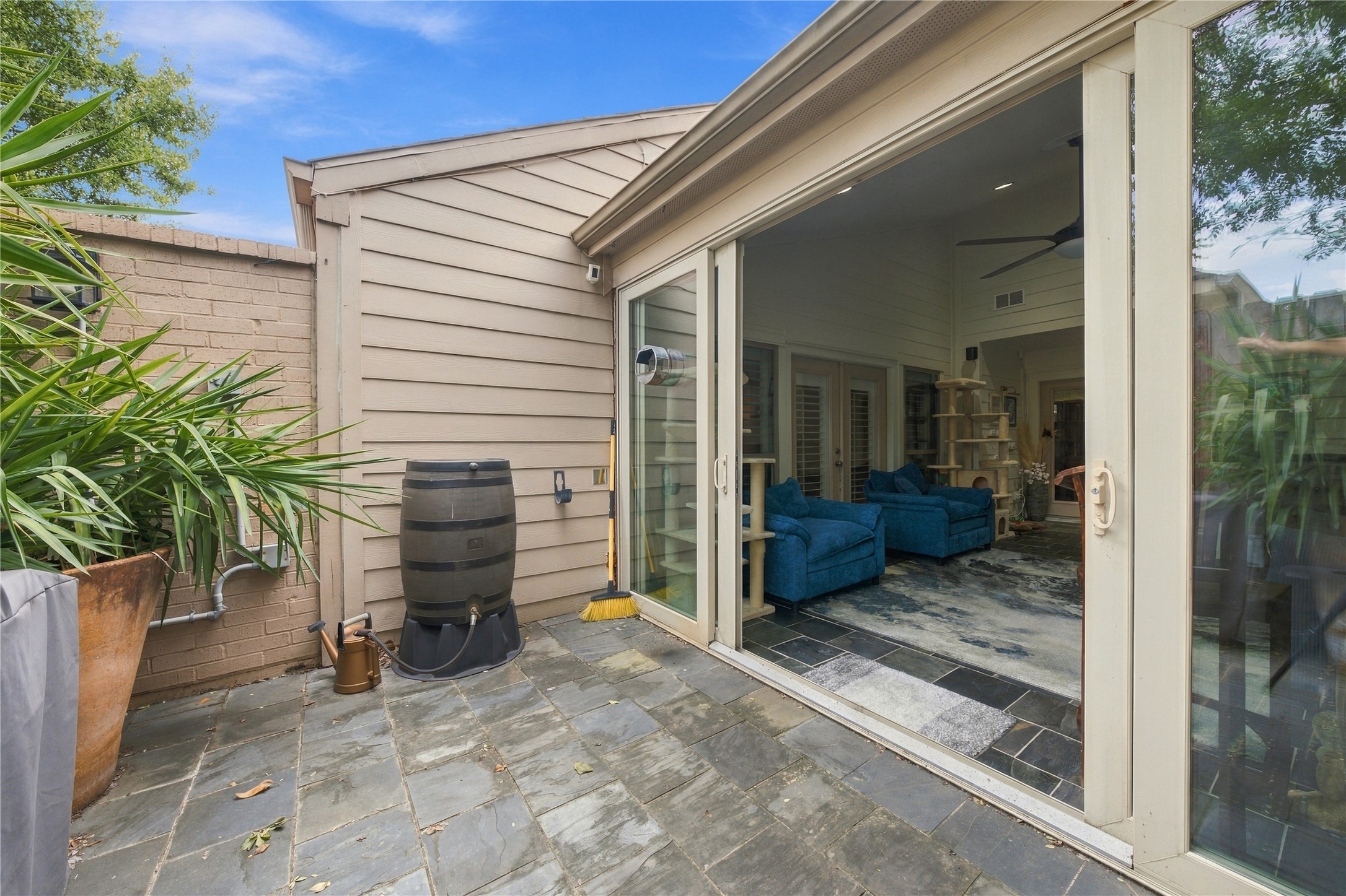 From outside, the sunroom's glass wall slides fully open onto slate pavers, while the privacy fence keeps this patio secluded.