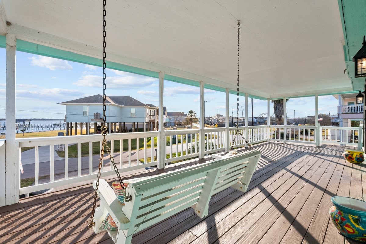This spacious covered porch features a wooden swing and offers an inviting view of a coastal neighborhood, perfect for enjoying outdoor relaxation.