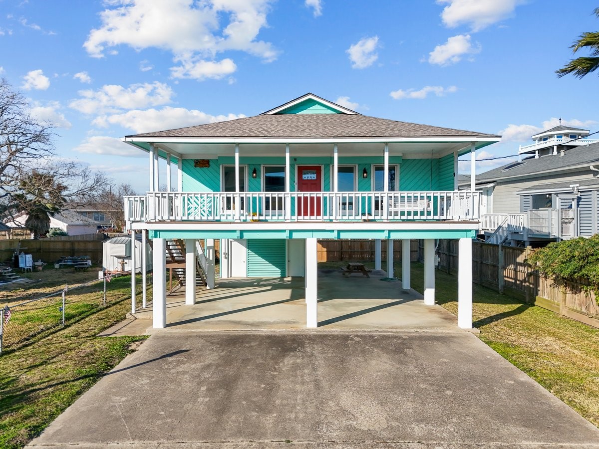 This elevated coastal home features a vibrant turquoise exterior, a spacious wraparound porch, and ample parking underneath. Ideal for enjoying seaside breezes and outdoor living.