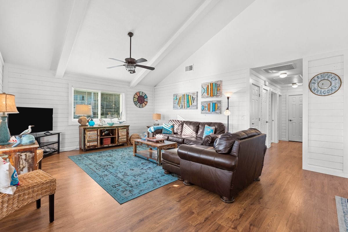 This inviting living room features vaulted ceilings, a ceiling fan, and abundant natural light. It boasts a cozy seating area with white shiplap walls to enhance the airy, coastal vibe. This inviting living room features vaulted ceilings, a ceiling fan, and abundant natural light. It boasts a cozy seating area with white shiplap walls to enhance the airy, coastal vibe.