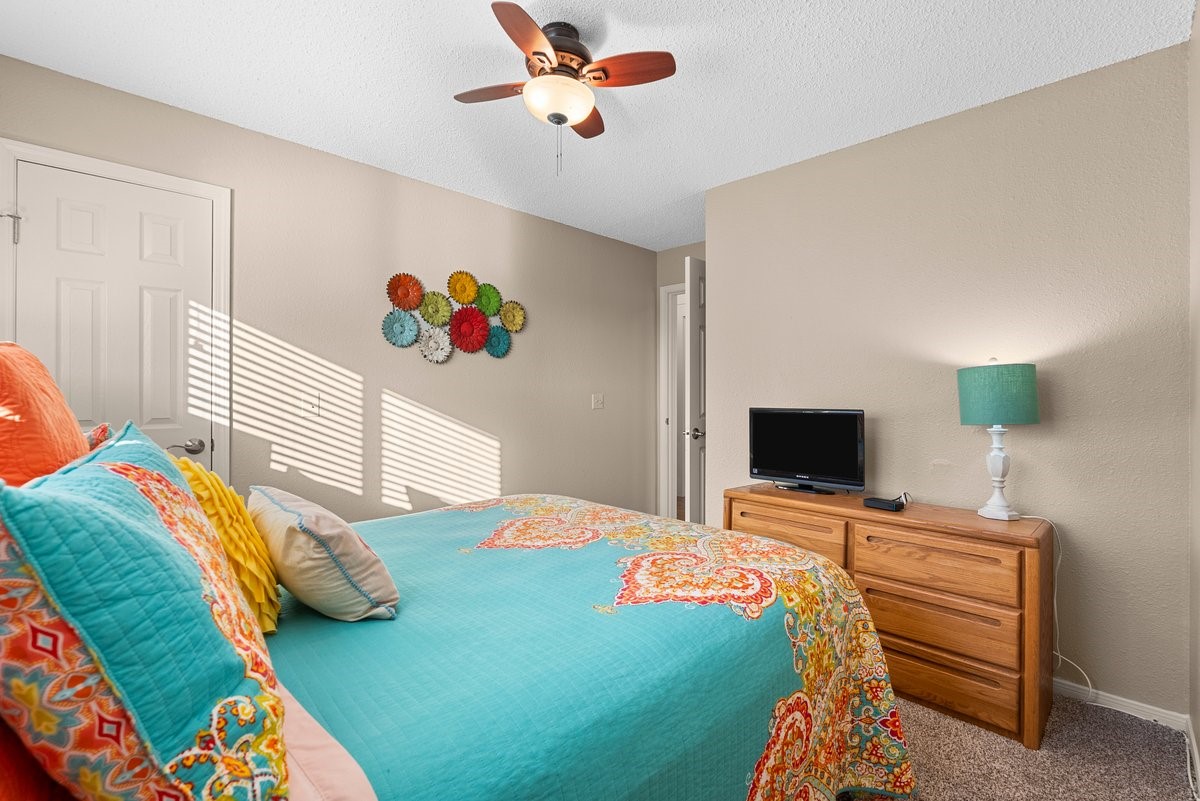 This cozy bedroom features warm beige walls and a colorful bedspread, creating a vibrant, inviting atmosphere. The room includes a ceiling fan offering both comfort and style. This cozy bedroom features warm beige walls and a colorful bedspread, creating a vibrant, inviting atmosphere. The room includes a ceiling fan offering both comfort and style.