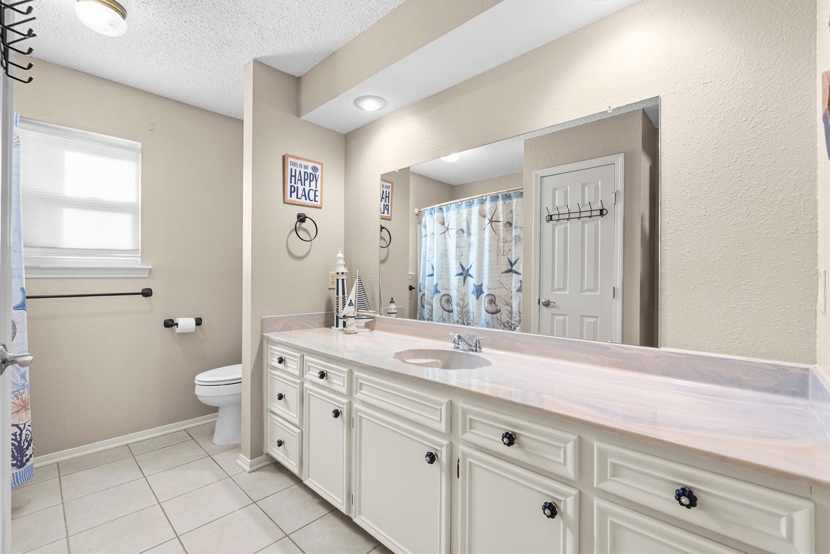 Bright and spacious bathroom with neutral tones, featuring a large mirror, ample counter space, and a decorative shower curtain. Ideal for comfort and style.