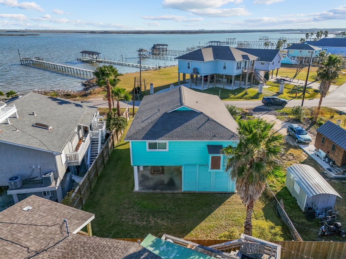 This photo showcases a charming waterfront home with a spacious yard, nestled near a serene body of water. The property includes a dock, offering direct access to the water, and is surrounded by other elevated homes, providing a picturesque coastal community vibe.