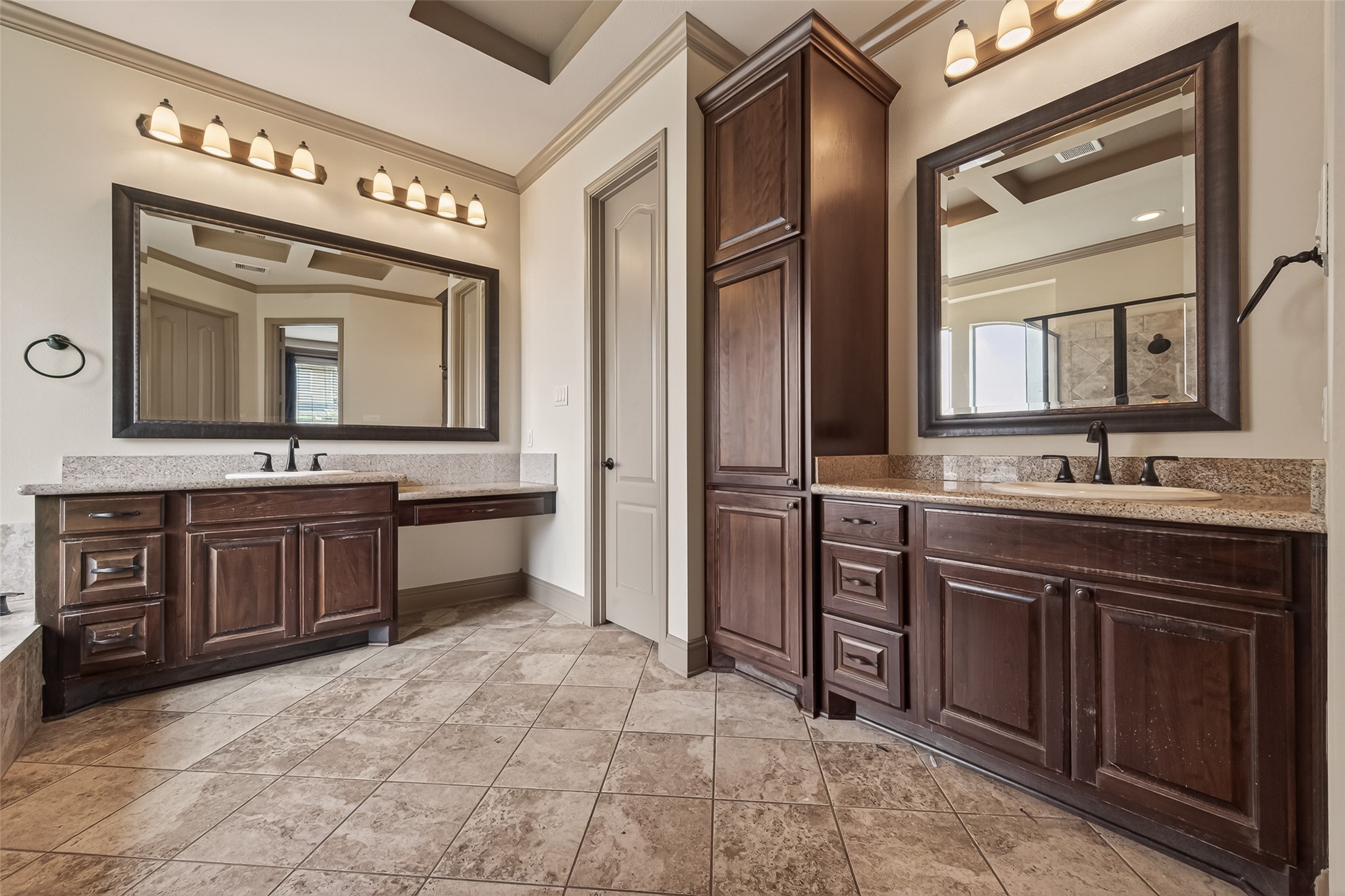 Dual vanities with granite countertops and framed mirrors provide ample space for morning routines. A floor to ceiling wood linen tower between the vanities adds abundant storage. Oil rubbed bronze fixtures and warm vanity lighting complement the rich cabinetry, creating a sophisticated and well appointed retreat.