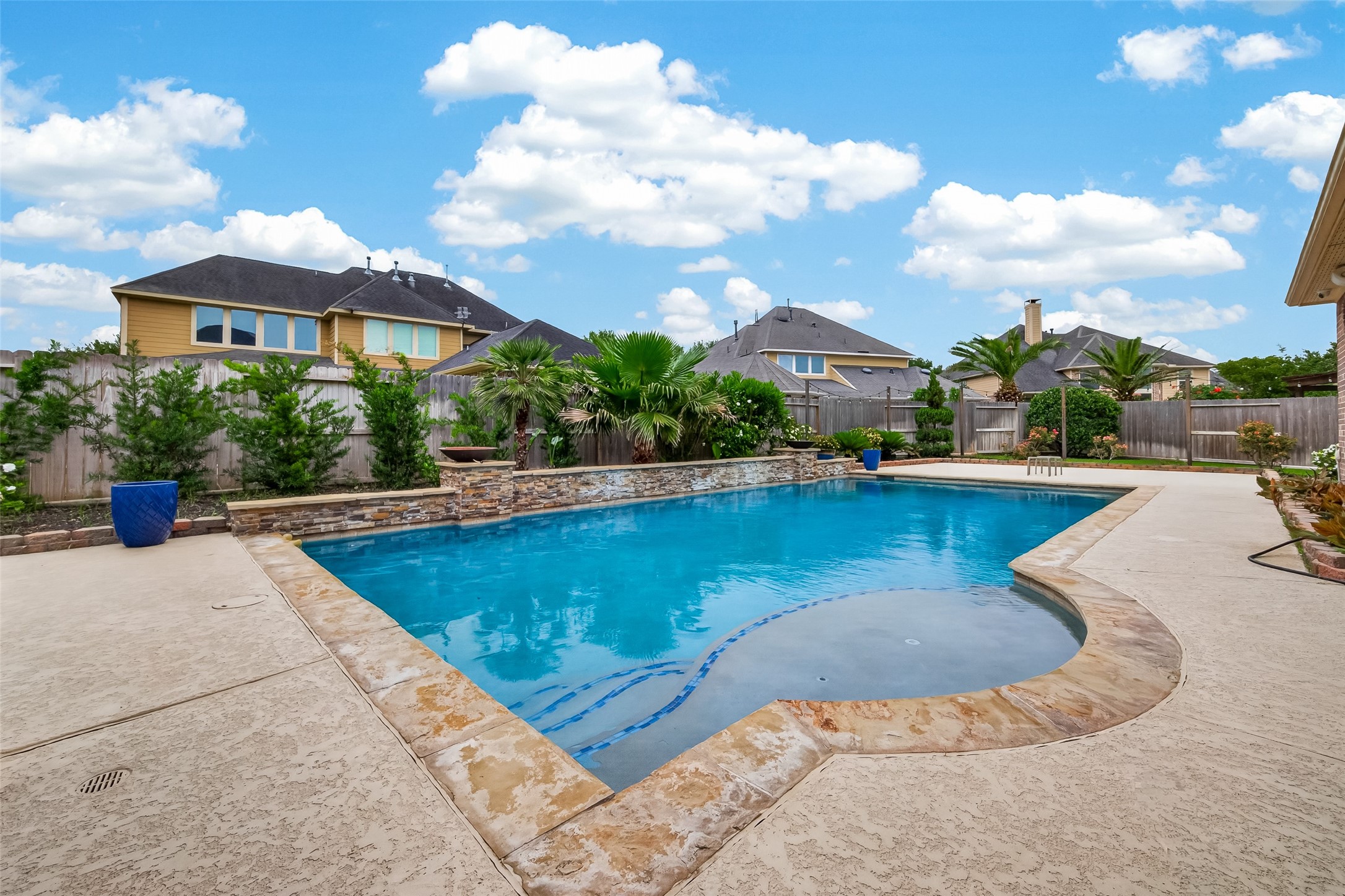 Step into your own backyard oasis, where a sparkling pool with a beautiful stone coping surround invites warm-weather enjoyment. Lush tropical landscaping, including mature palm trees and evergreen shrubs, frames the fully fenced yard, creating a private and resort-like atmosphere. The generous pool deck provides ample space for lounge chairs and outdoor entertaining under the open Texas sky.
