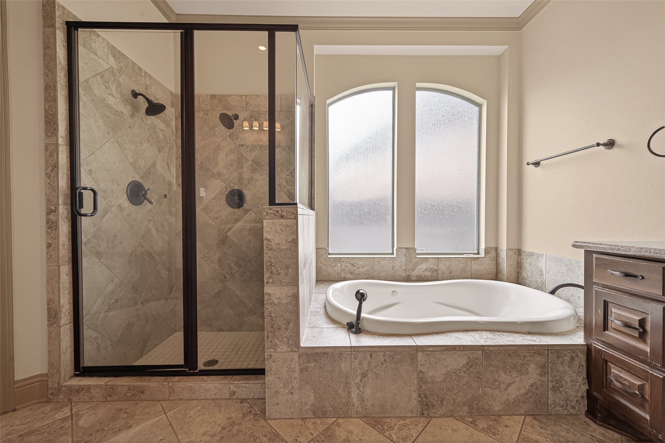 The tile surrounded soaking tub is nestled beneath an elegant arched privacy window that fills the space with soft, natural light. Adjacent to the tub, the glass enclosed shower features diagonal tile work, oil rubbed bronze fixtures, and a built in niche for convenience. This spa like setup offers the best of both worlds for relaxation and daily use.