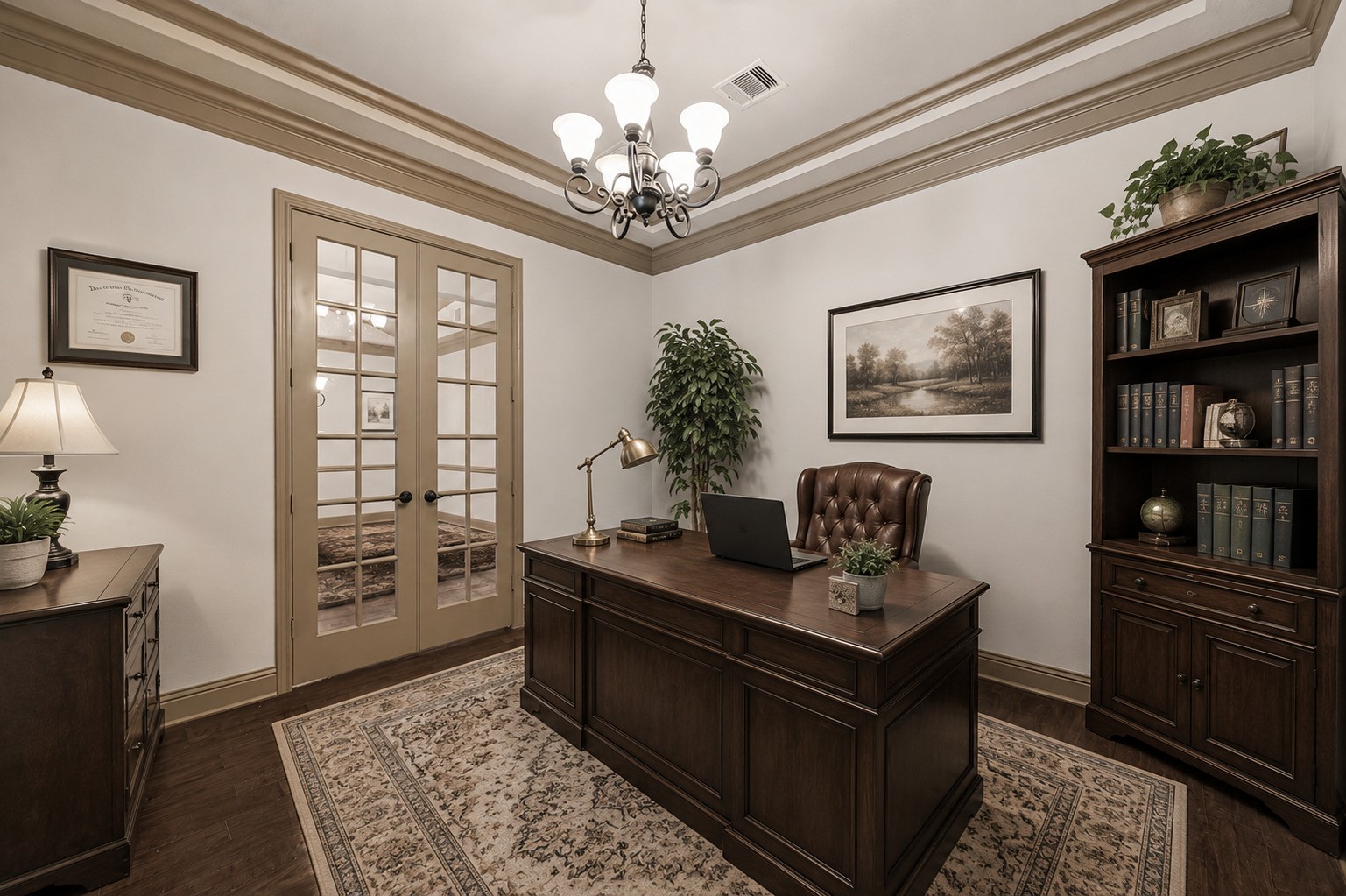 The dedicated home office combines functionality with refined style, featuring a tray ceiling with crown molding, a chandelier, and hardwood flooring throughout. Elegant French doors provide a charming entrance while allowing light to flow between spaces. This versatile room is ideal for working remotely, pursuing personal projects, or simply enjoying a quiet area to focus. The warm neutral palette and tasteful molding details create a productive yet comfortable workspace. Virtually staged.