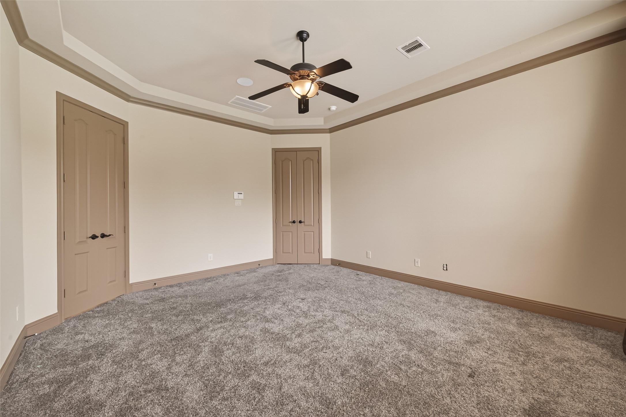 This spacious primary bedroom offers a peaceful retreat with plush carpeting, a lovely tray ceiling with crown molding, and a ceiling fan for year-round comfort. The generous layout provides endless possibilities for furniture arrangements, while two doors offer access to the primary bathroom and closet, adding both privacy and convenience.