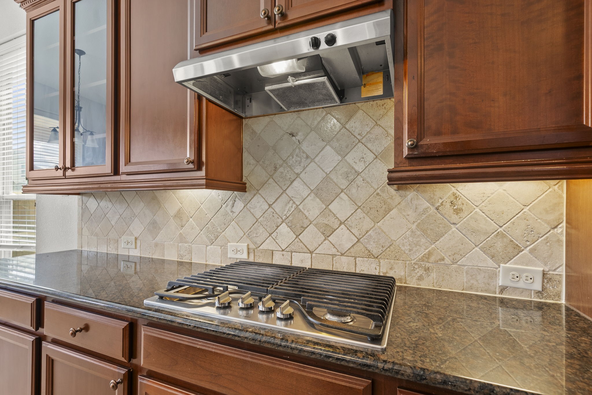 Gourmet gas cooktop is beautifully framed by an elegant travertine backsplash and gleaming granite counters, a chef's dream come true!