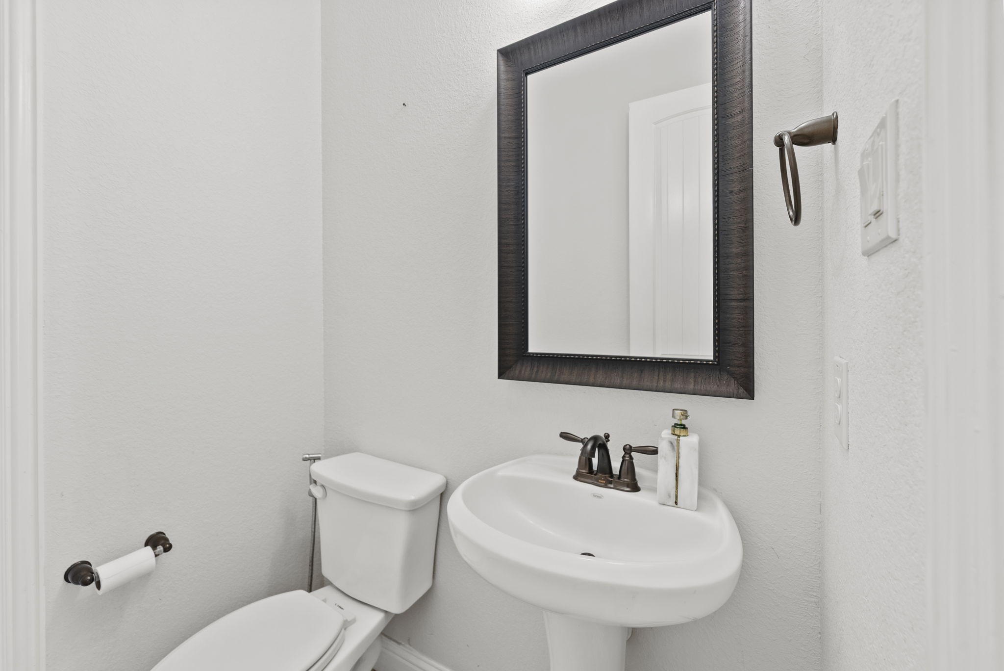 Charming half bath with pedestal sink, framed mirror, and classic fixtures in a clean, minimalist layout.