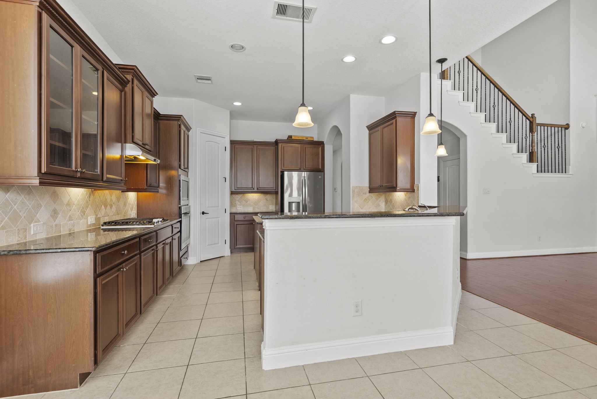 Open concept kitchen flows effortlessly into the grand staircase and living room, complete with pendant lighting, granite counters, and abundant cabinet storage!