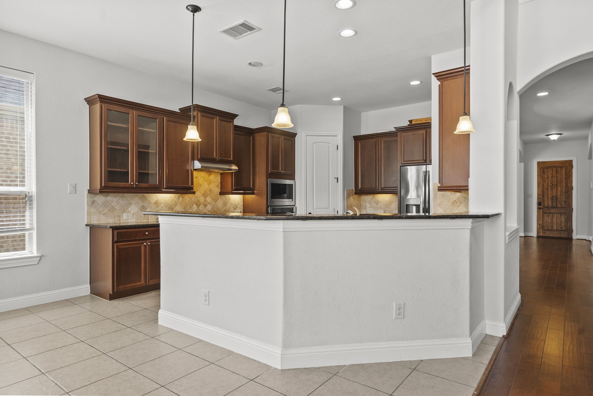 Spacious kitchen bar seating overlooks a beautifully appointed workspace with rich cabinetry, stylish pendant lighting, and easy flow into the home's hardwood-lined hallway!