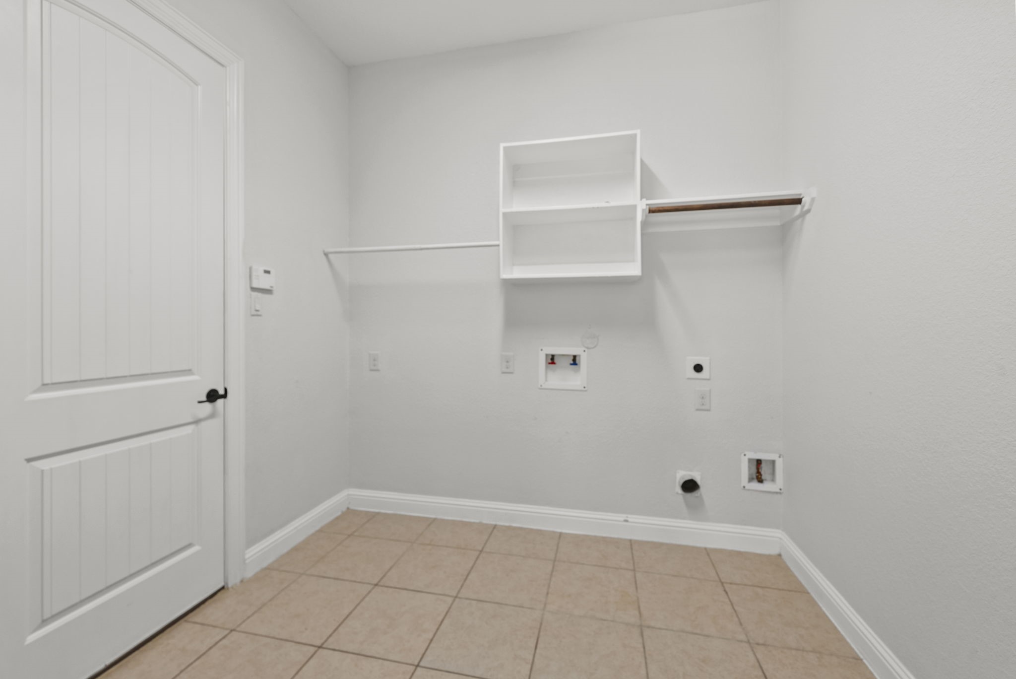 Convenient dedicated laundry room offers built-in shelving and hanging space, practical, everyday functionality with a tidy tile floor!