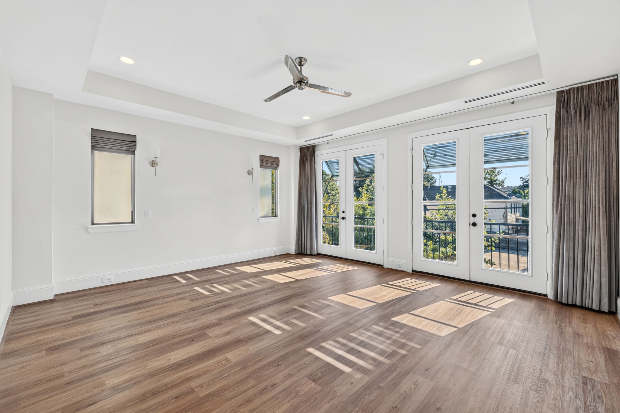 Broad French doors open to the upper level juliette balcony, flooding the primary suite with light
