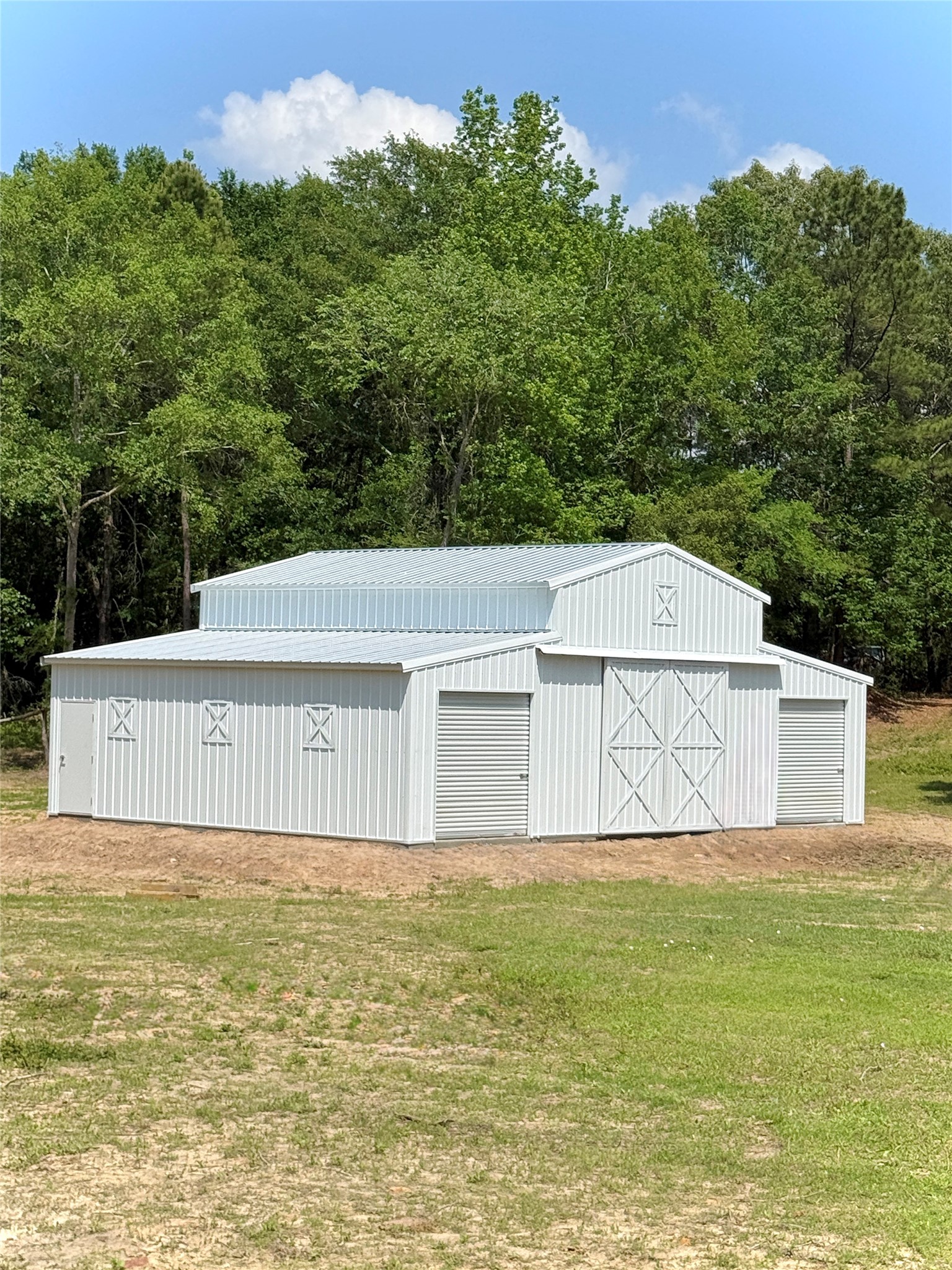 Spacious metal barn with rolling doors and classic design, set against lush greenery, perfect for storage or equestrian needs. Spacious metal barn with rolling doors and classic design, set against lush greenery, perfect for storage or equestrian needs.