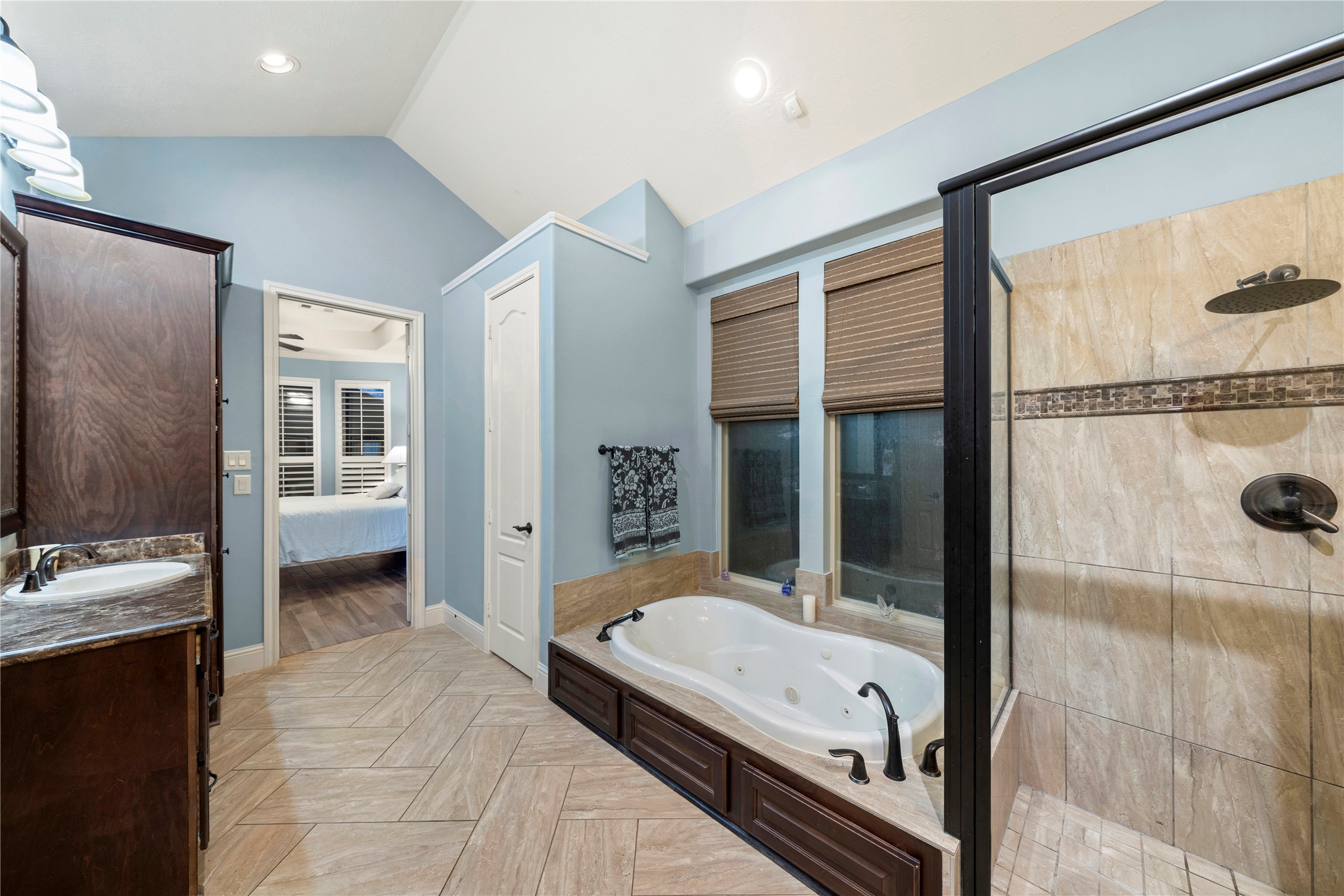 Experience luxury in this elegant bathroom featuring a spacious glass-enclosed shower, a relaxing jetted tub, and stylish tile flooring. The room is enhanced by ample natural light and tasteful cabinetry, creating a serene retreat.