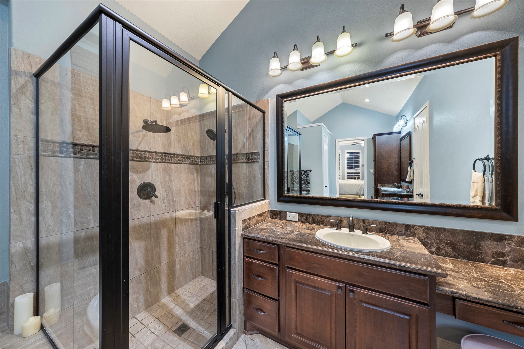 Elegant bathroom featuring a spacious glass-enclosed shower, rich wood cabinetry, and  sleek granite countertops with dual vanities.