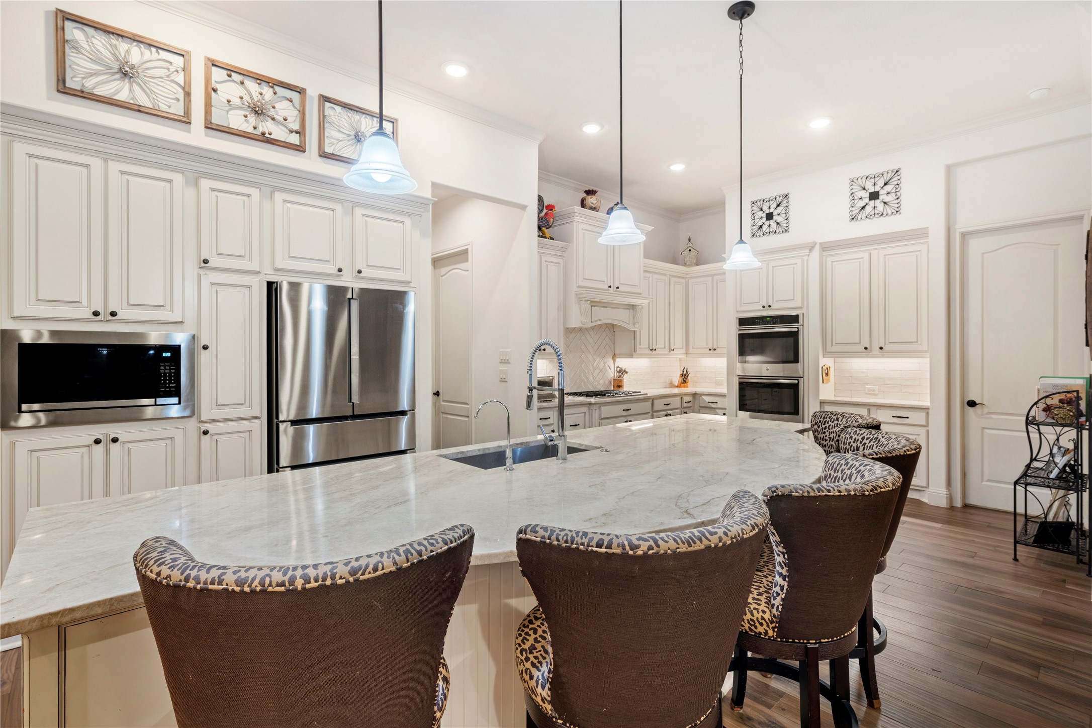 Elegant kitchen featuring a large marble island with seating, stainless steel appliances, and custom cabinetry, all under stylish pendant lighting.