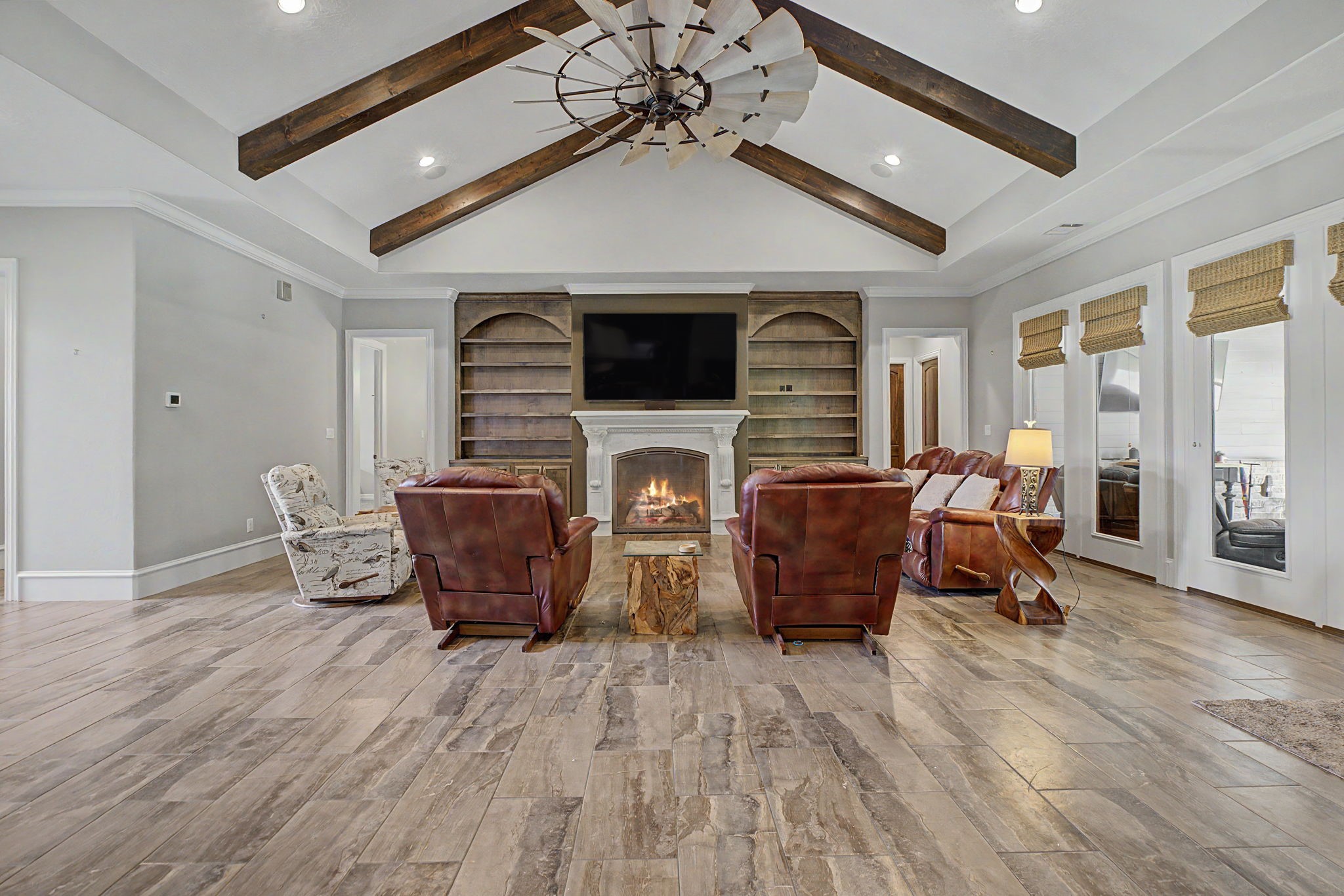 Alternate view of the living room showcasing the custom built-ins, stunning wood beams, and durable tile flooring. And don't miss the impressive statement ceiling fan overhead! Alternate view of the living room showcasing the custom built-ins, stunning wood beams, and durable tile flooring. And don't miss the impressive statement ceiling fan overhead!